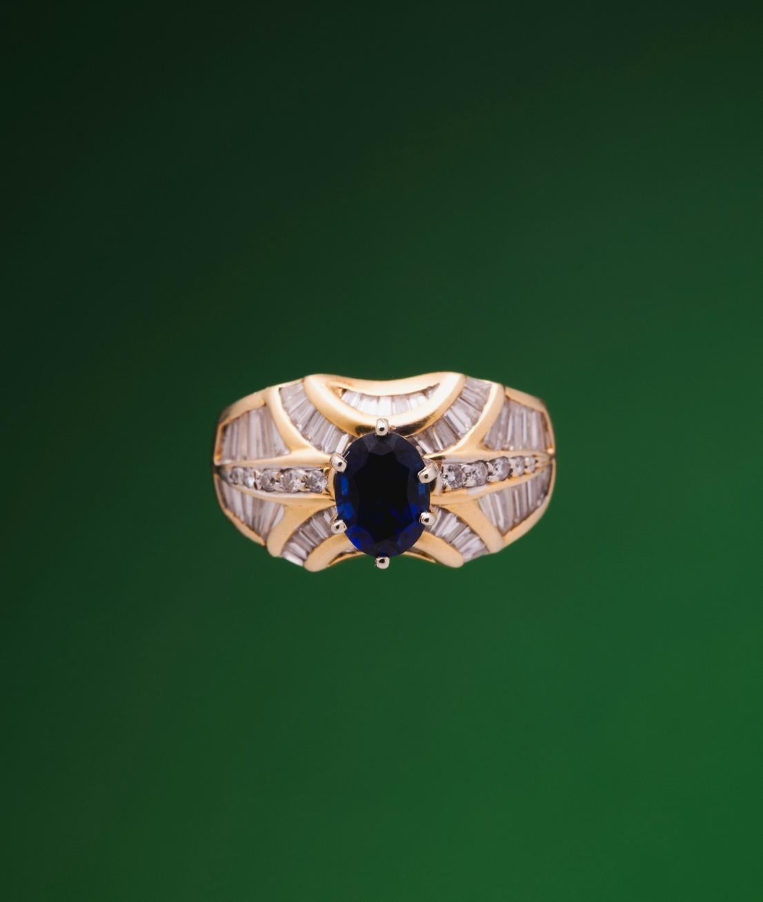 This Ring is a 18k yellow gold ring of 12 grams weight piece, filled with baguette diamonds, and a oval sapphire of 1 carat is antique design.