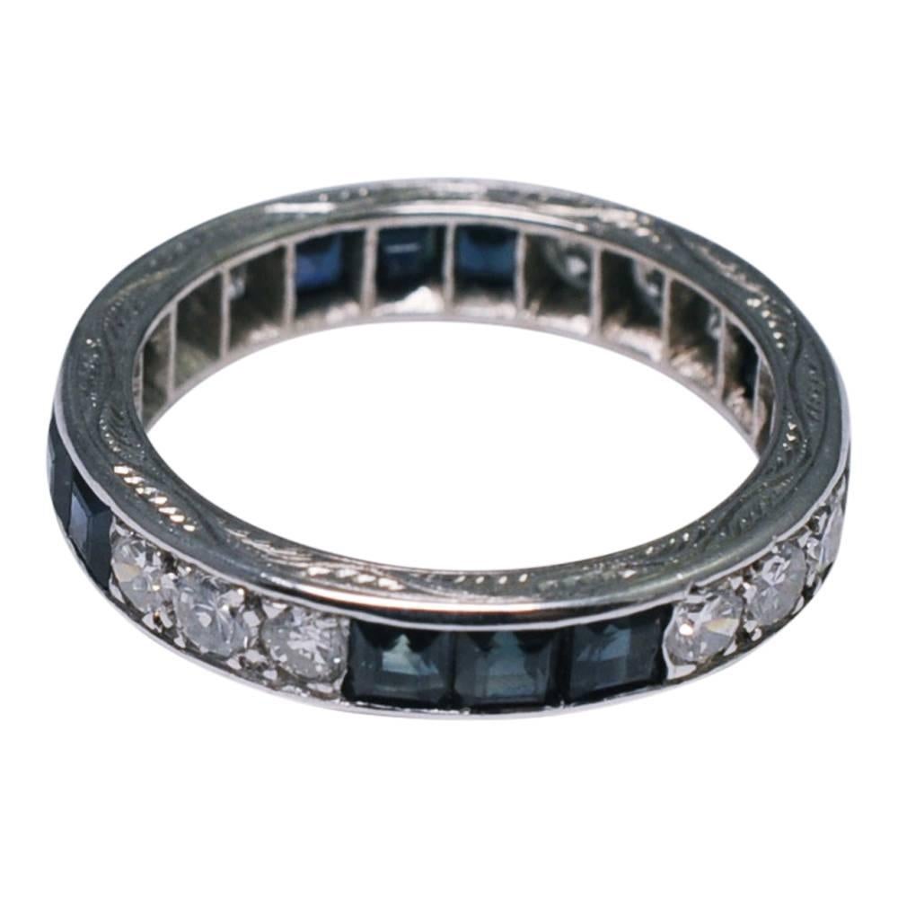 Art Deco sapphire and diamond eternity ring; the square cut sapphires weigh 2.40ct, the transitional cut diamonds weigh 1.20ct.  The ring tests as 18ct gold and is ornately engraved on the top and base.  Weight 4.6gms.  Depth 4mm .  C.1930.  Finger