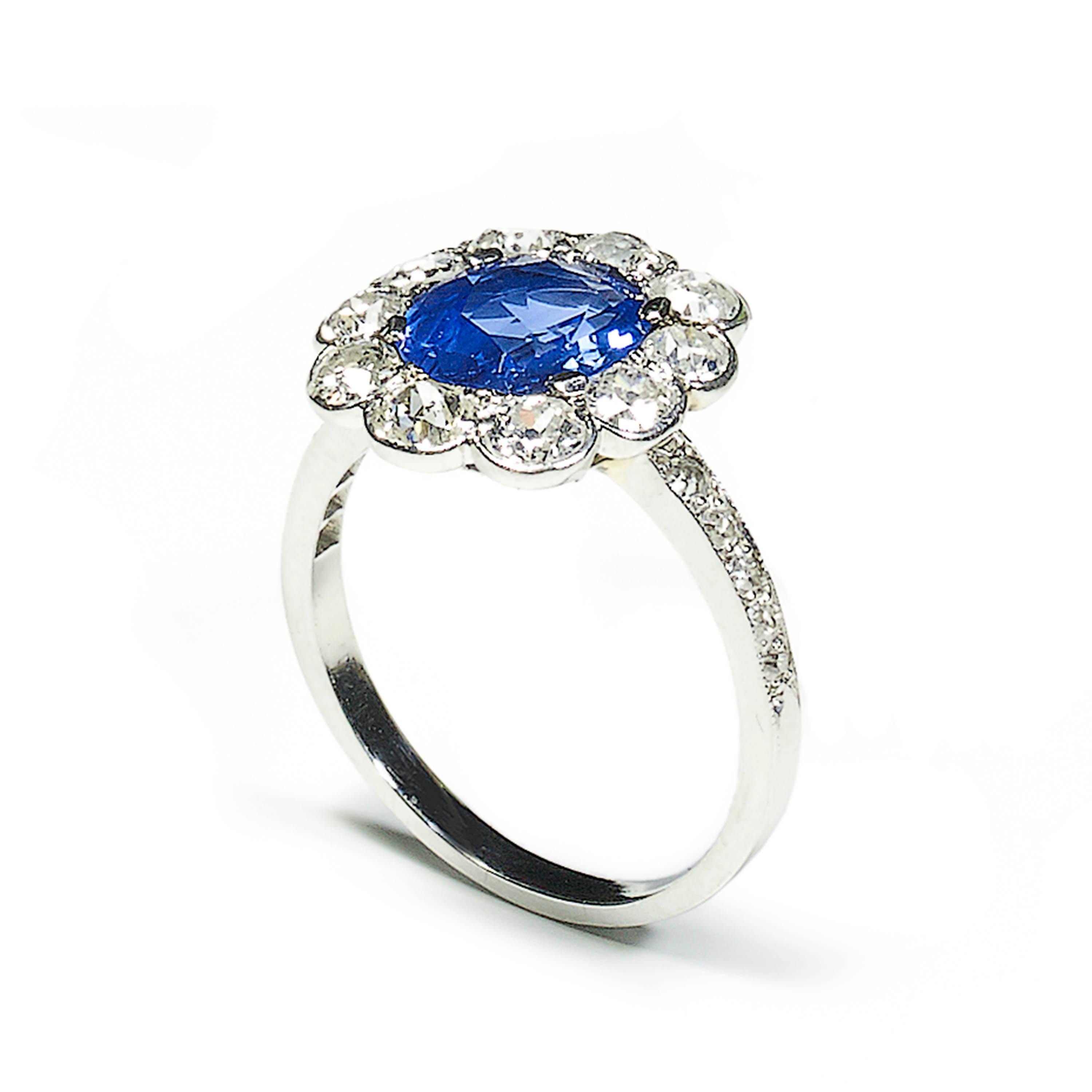 A French sapphire and diamond cluster ring, set with an approximately 1.72ct, unheated, oval, native-cut, Ceylon sapphire in a four claw setting, surrounded by ten, old-cut diamonds in grain and rub over settings, with eight-cut diamonds set in