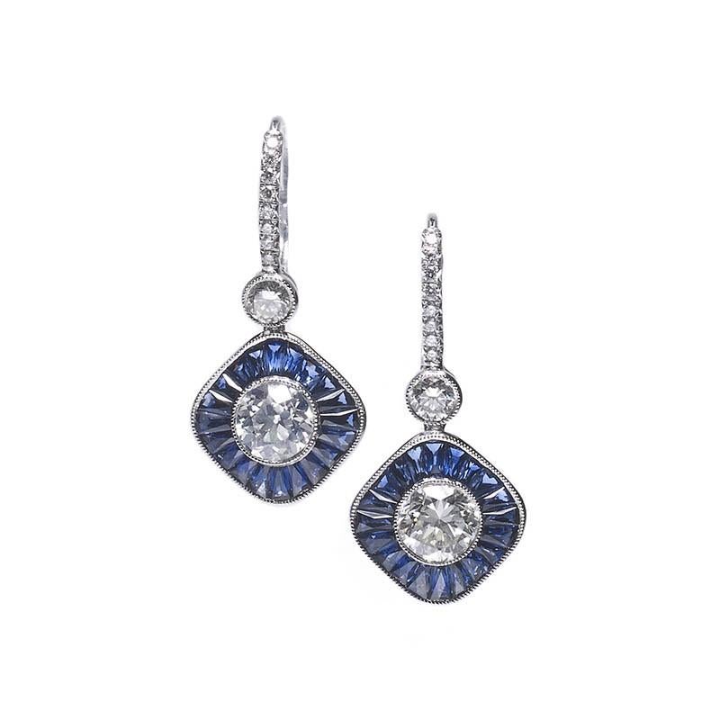 A pair of sapphire and diamond cluster drop earrings, mounted in platinum, each set with a round diamond to the centre with a millegrain edge, surrounded by a cluster of tapered sapphires, topped with a single round brilliant-cut diamond, and