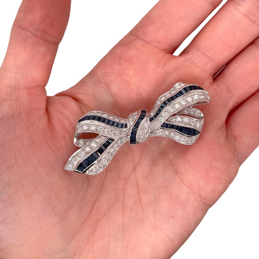 Antique motif sapphire and diamond bow ribbon brooch in 18k white gold. Brooch contains sapphire baguettes, 3.20tcw and round brilliant diamonds, 2.20tcw. Diamonds are near colorless and SI1 in clarity. All stones are mounted in a handmade channel