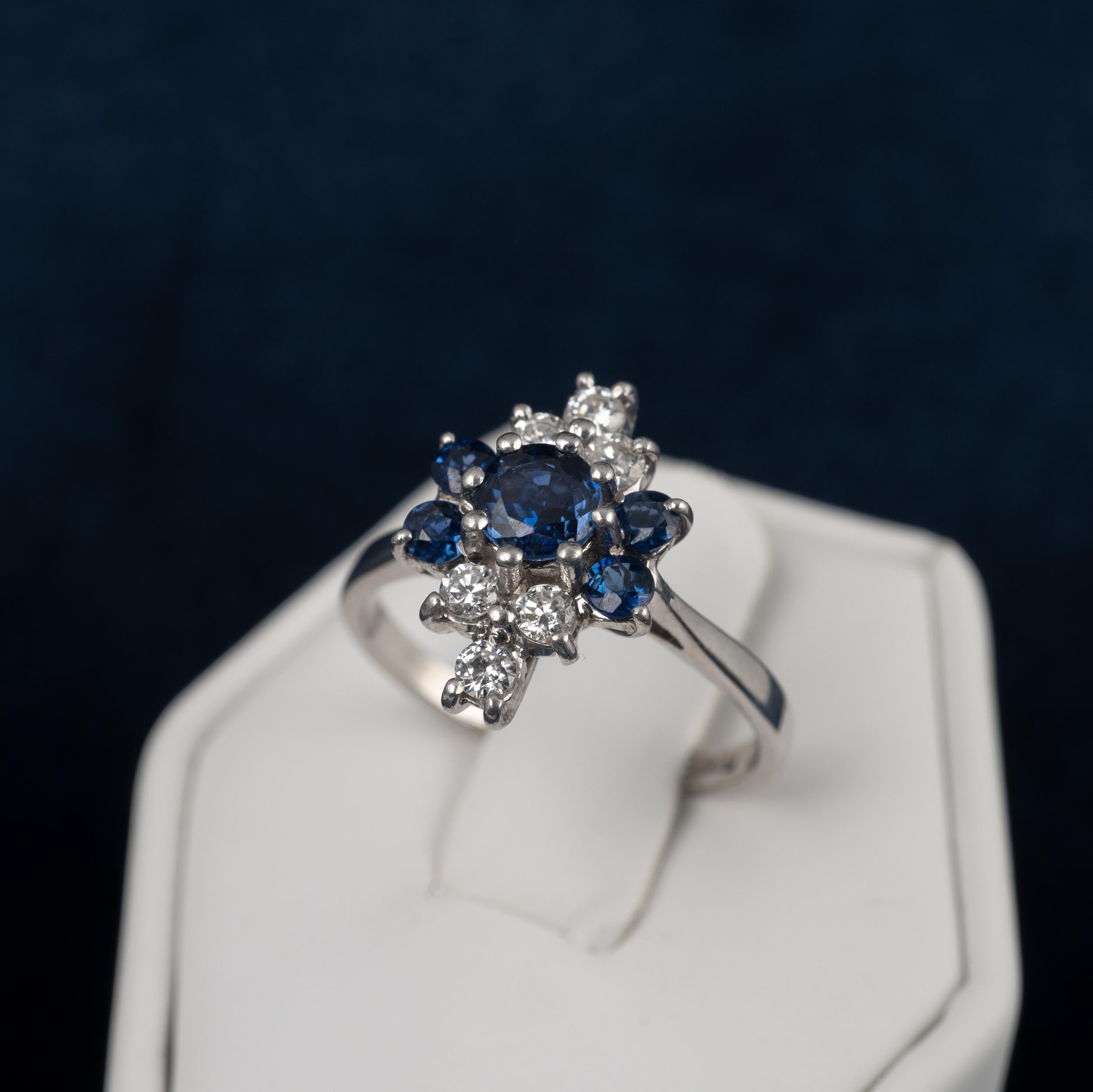 A beautiful and striking sapphire diamond cluster ring crafted in 18 karat white gold.

A central round cut 0.35-carat sapphire is flanked each side by a pair of smaller matching sapphires of 0.06cts each. To complement the rich blue of the