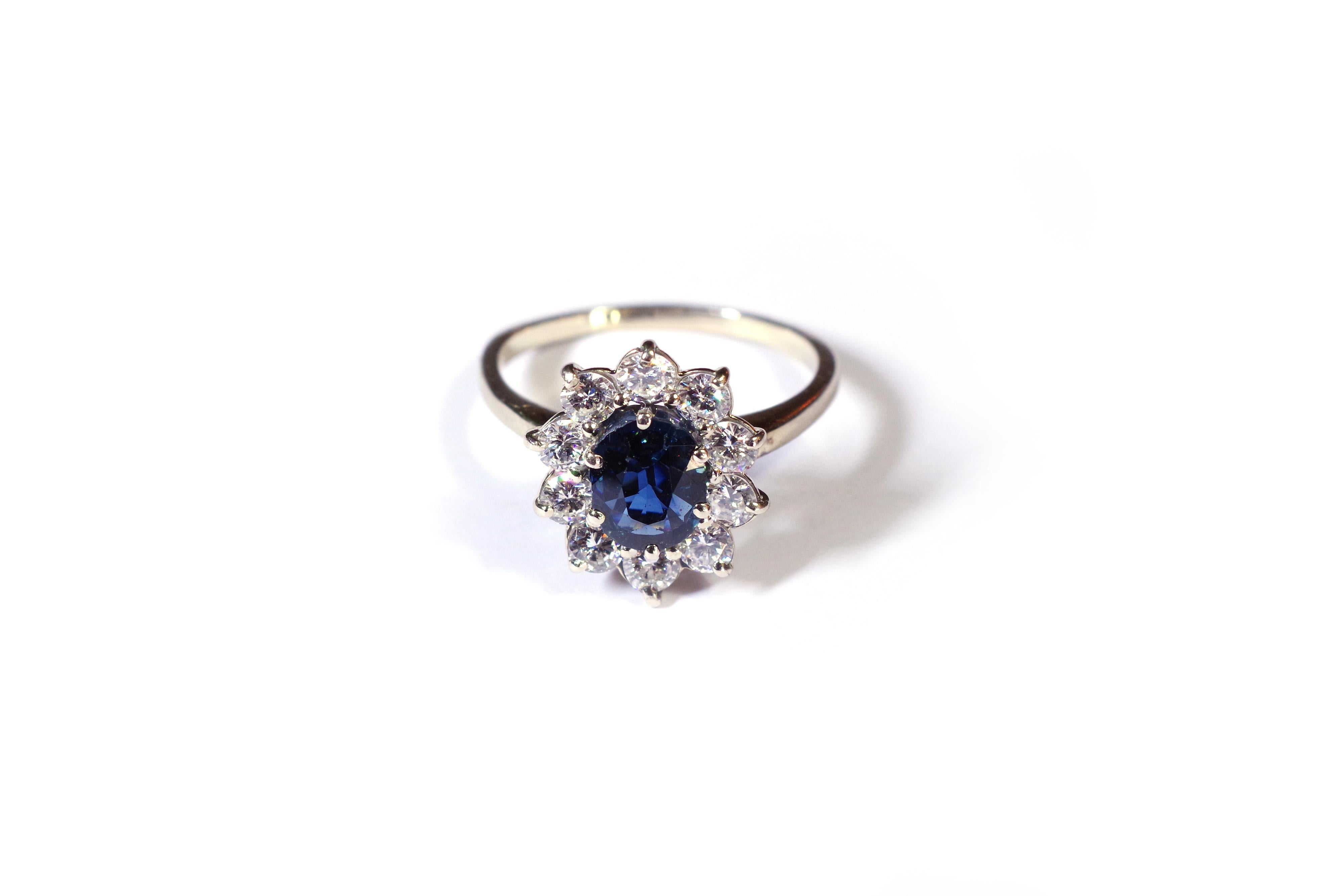 Sapphire diamond cluster ring in white gold 18 karats. The bezel is set with an oval cut sapphire surrounded by 10 brilliant-cut diamonds. The sapphire is set with six claws and has a beautiful deep blue colour. Second hand engagement ring, circa