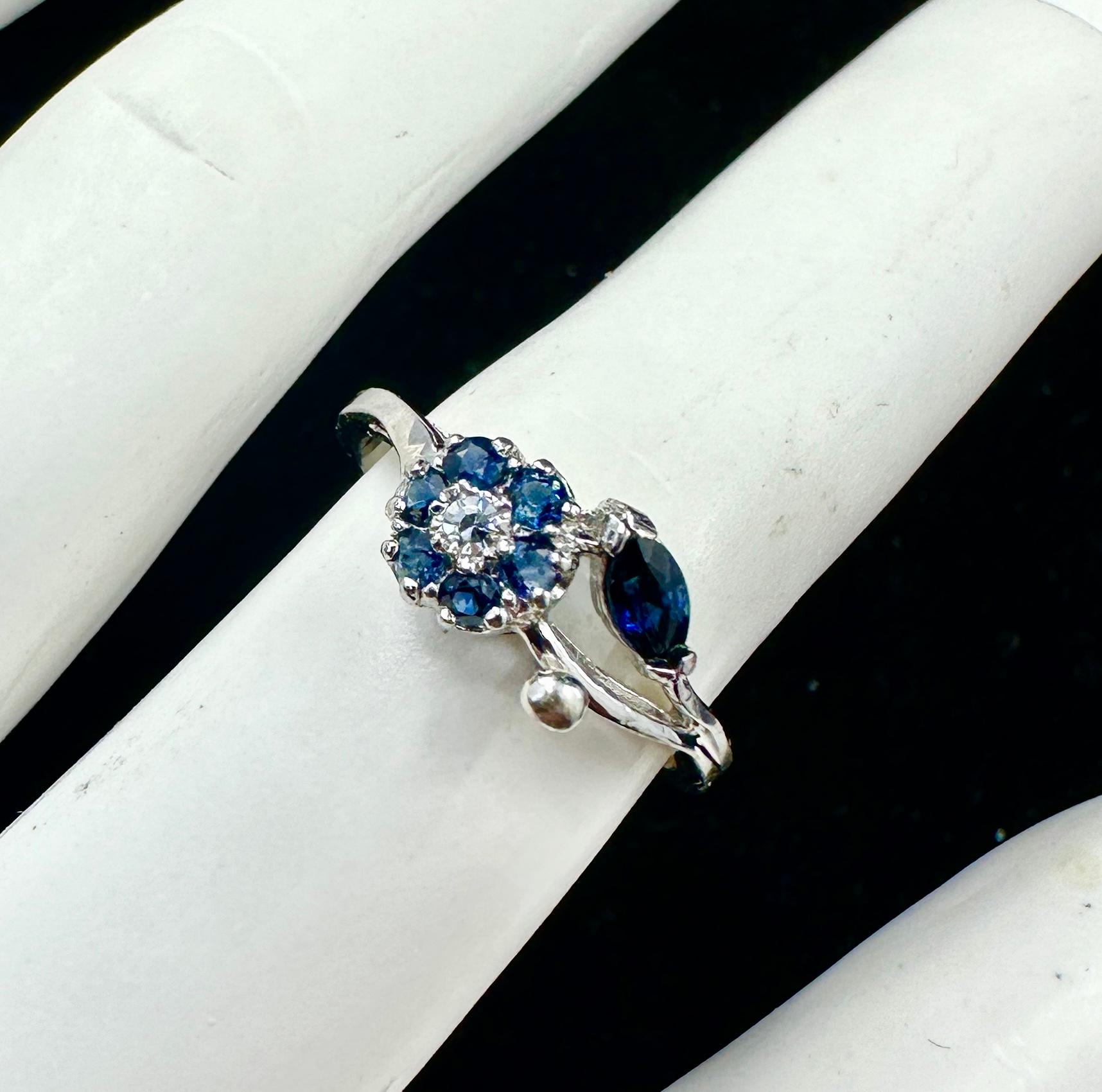 Questo è uno splendido e romanticissimo anello antico con zaffiro e diamante in oro bianco 14 carati con un delicato motivo floreale.  La combinazione di zaffiri e diamanti in questo splendido anello è una delizia assoluta.  Il fiore è centrato da
