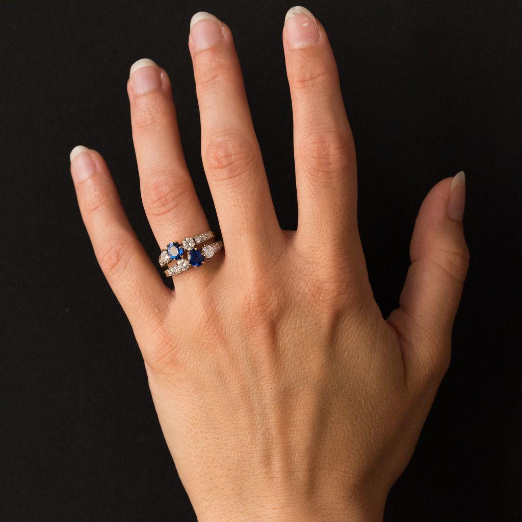 Ring in 18 carat yellow gold and platinium, eagle and dog heads hallmarks. 
Formed of a double ring, this ravishing sapphire lovers ring is set with 2 claw set oval blue sapphires each accentuated by a diamond at each side and by a row of 3 pave