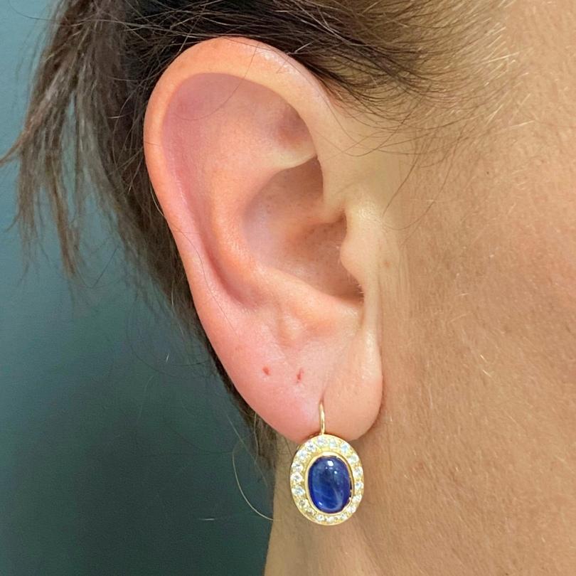 A pair of classic sapphire diamond halo earrings made of 14k gold.
The sapphires cabochons’ velvety appearance is enhanced with the diamond frame and
brightness of the yellow gold. A lever back closure allows these sapphire earrings to
