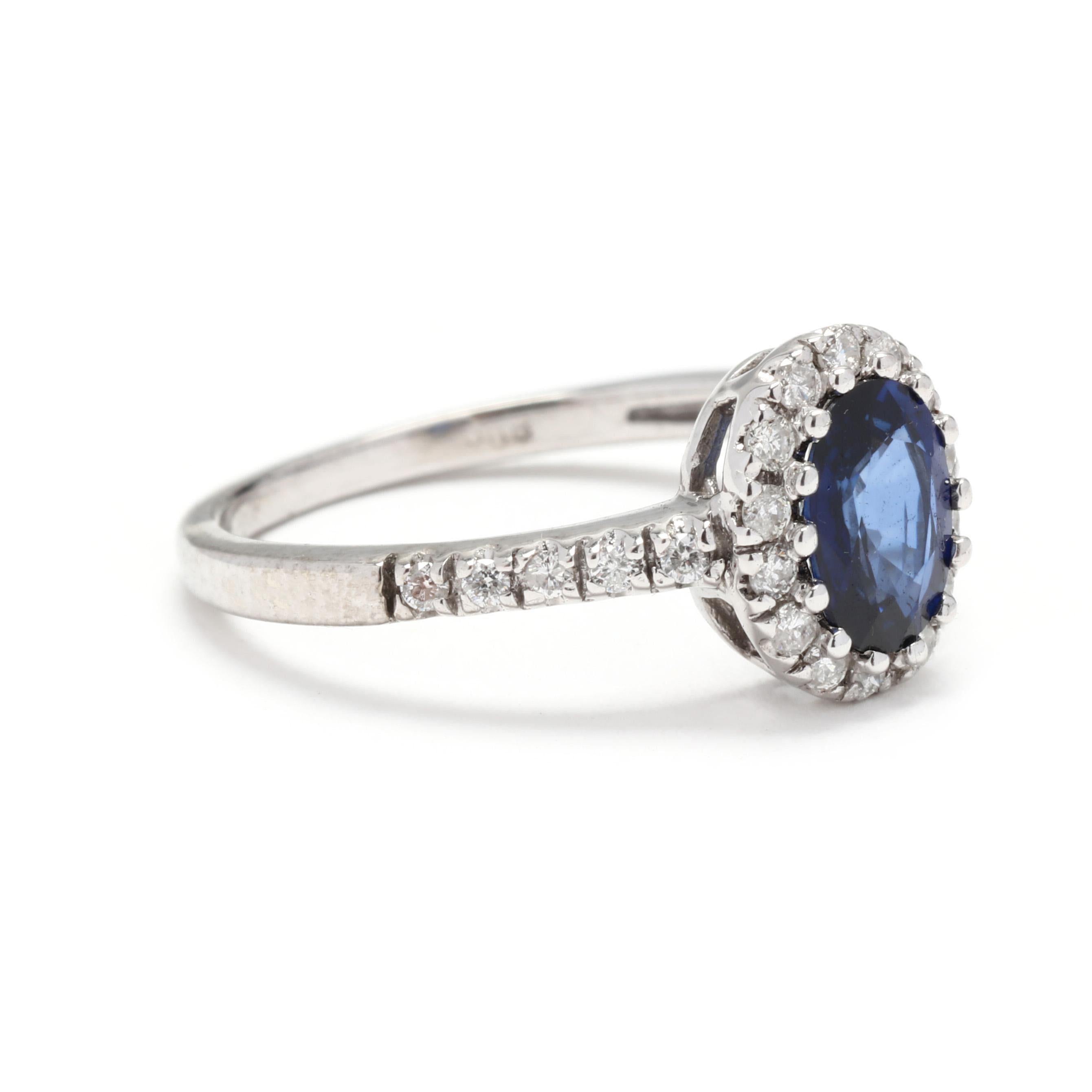 A 14 karat white gold sapphire and diamond halo engagement ring. This natural sapphire ring features an oval cut blue sapphire weighing approximately 1.10 carat surrounded by a halo of round brilliant cut diamonds and down the band weighing