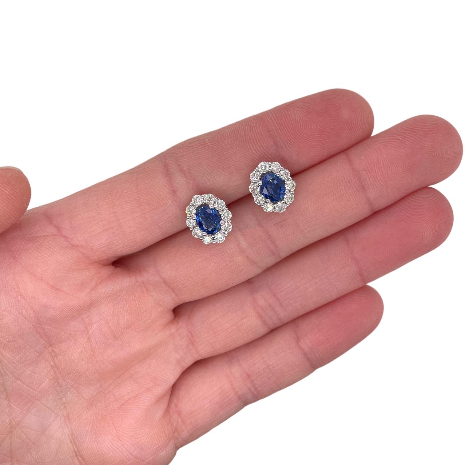 Pequeños pendientes con 2 zafiros azules ovalados de talla brillante finamente emparejados, 1,80 qt. Alrededor de los zafiros hay diamantes brillantes redondos que crean un halo, con un total de 1,05 tcw. Los diamantes son incoloros y de claridad