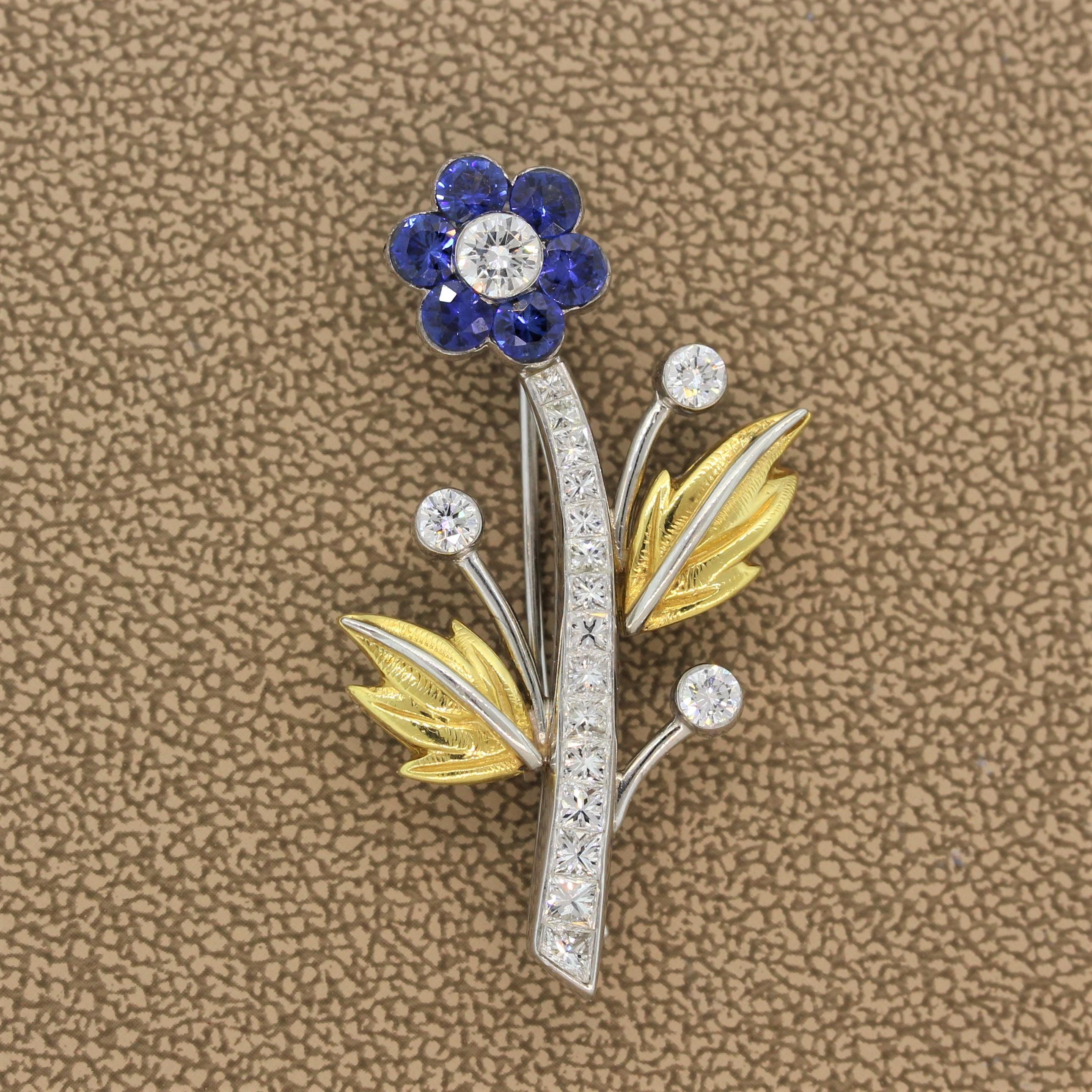 A flower brooch featuring 1.50 carats of round cut blue sapphires set as petals and 1.85 carats of round cut diamonds set on the stem, pistil and accenting leaves. The flower is set in platinum with two leaves made of 18K yellow gold with a soft