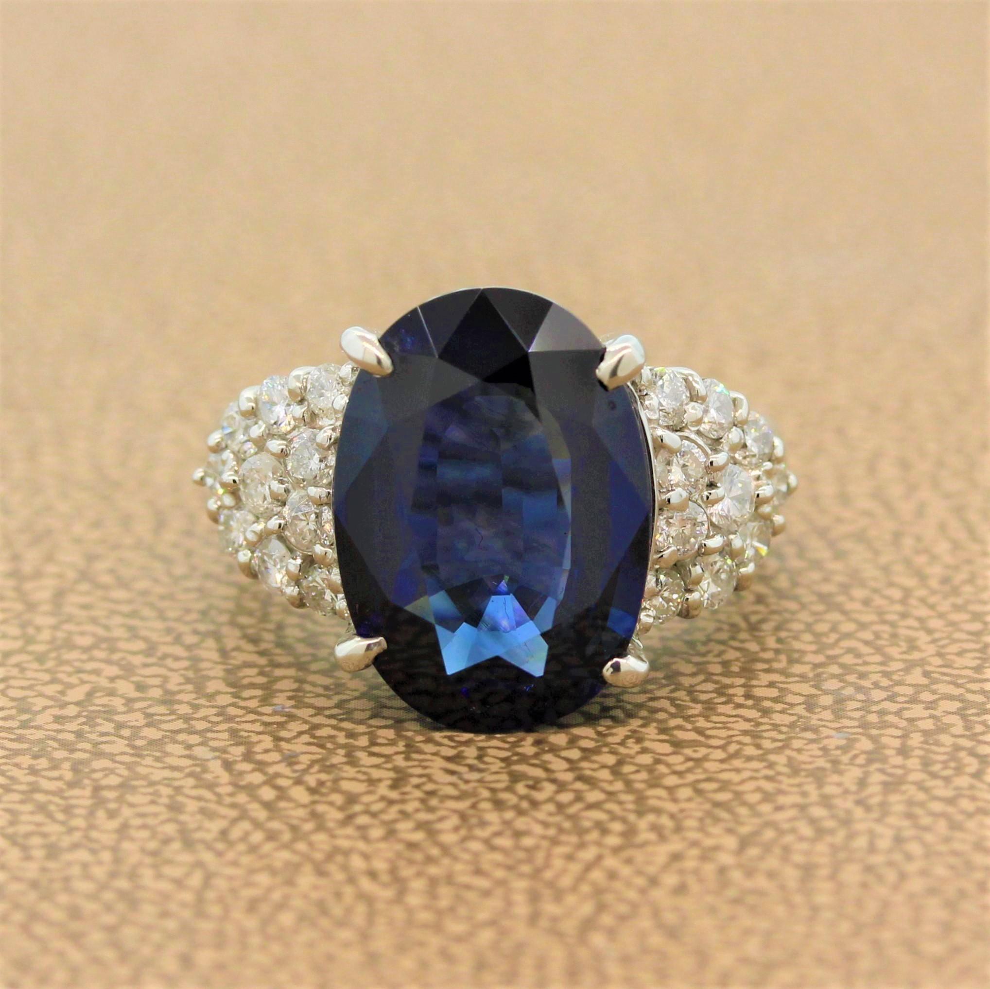 A gorgeous ring featuring a deep blue 8.24 carat oval shaped sapphire. The natural gemstone sits between two clusters of round brilliant cut diamonds in a classic prong setting. The accenting 1.03 carats of colorless diamonds add brilliance to this