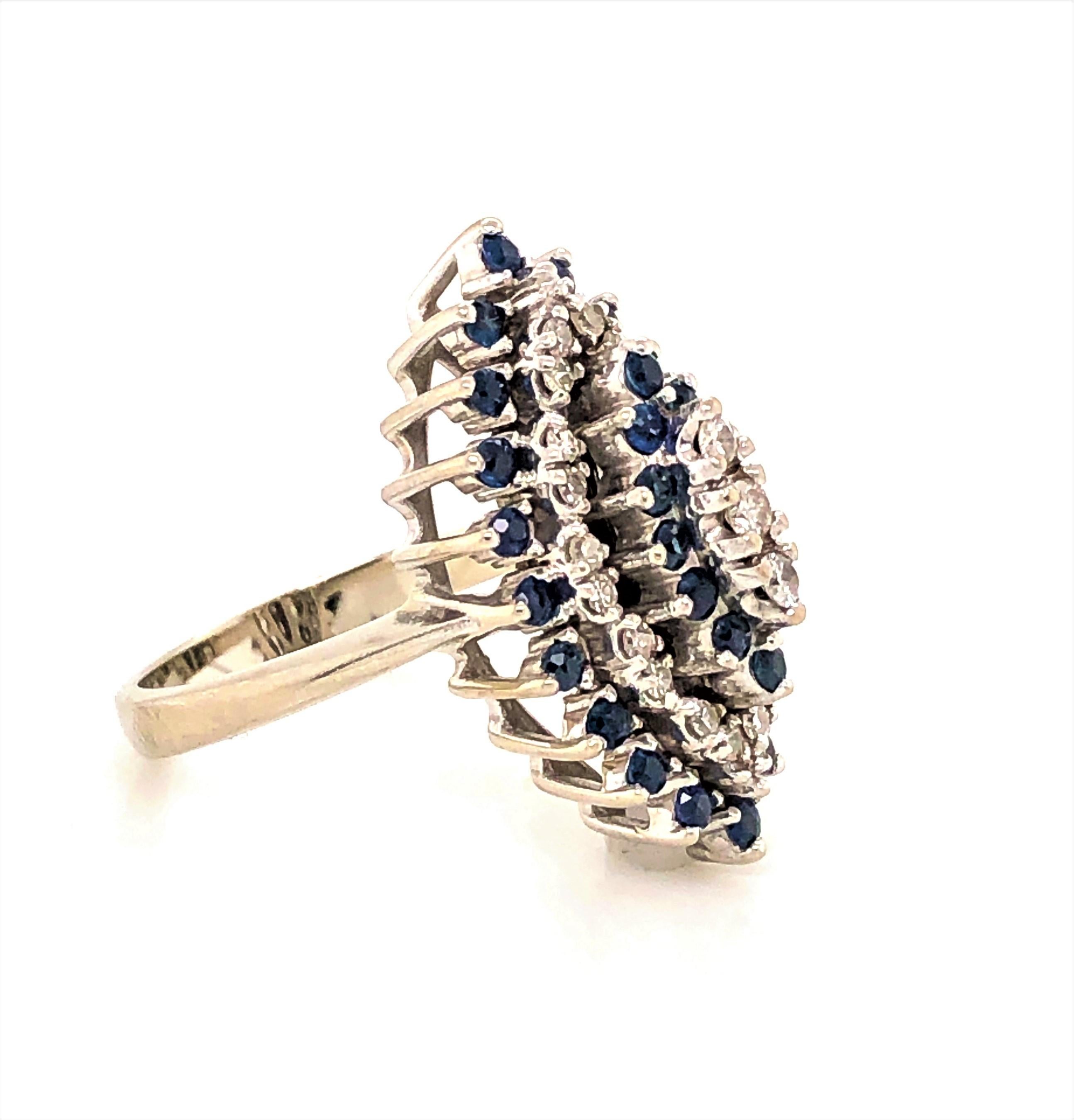 A pyramid of stunning blue ice with thirty two sapphires and twenty three diamonds all prong set in this oval fourteen carat 14K white gold cocktail ring. 
With a total carat weight of .32  sapphires and a total carat weight of  .23 faceted full cut
