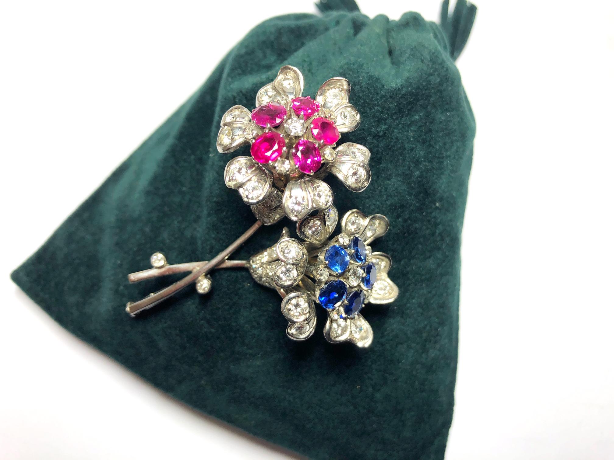 A vintage double headed flower brooch, set with round brilliant and eight-cut diamonds, with rubies in the centre of one flower and sapphires in the centre of the other, mounted in 14ct white gold.