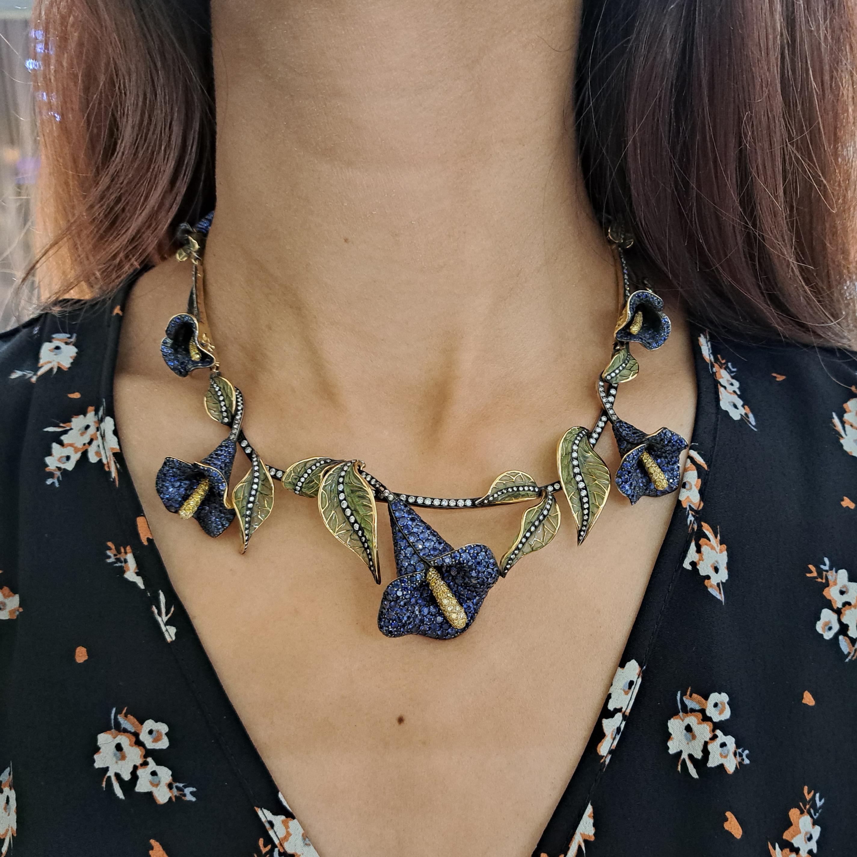 A modern, sapphire and diamond floral necklace, which is part of the MOIRA Collection, featuring calla lilies, which are pavé set with sapphires and yellow diamond set carpels, with stems which are set with round brilliant cut diamonds, with green