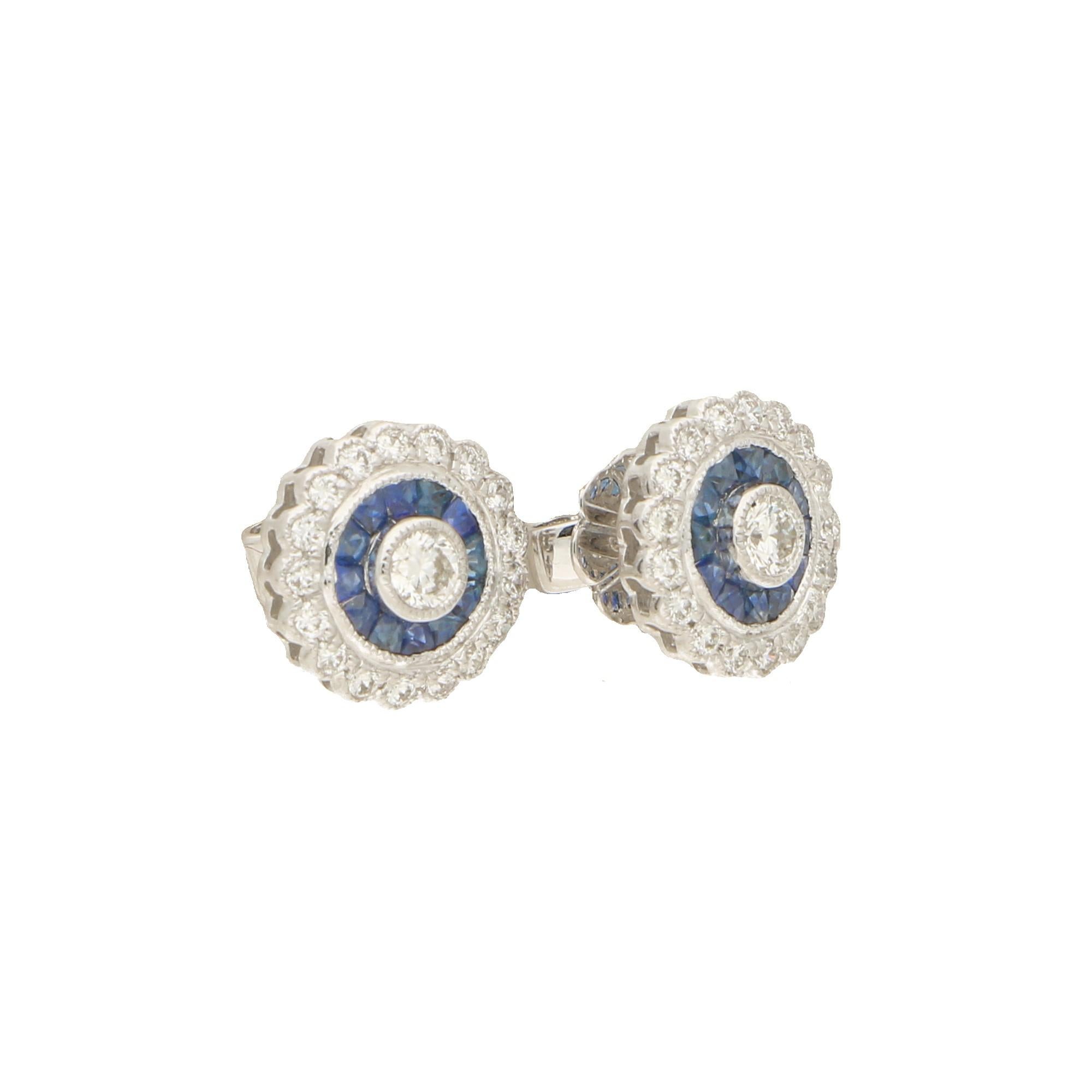 A spectacular pair of sapphire and diamond round target style earrings. 
A central round brilliant cut diamond is bezel set in 18ct white gold to a surround of French cut blue sapphires, which in turn is set to a surround of grain set diamonds, all