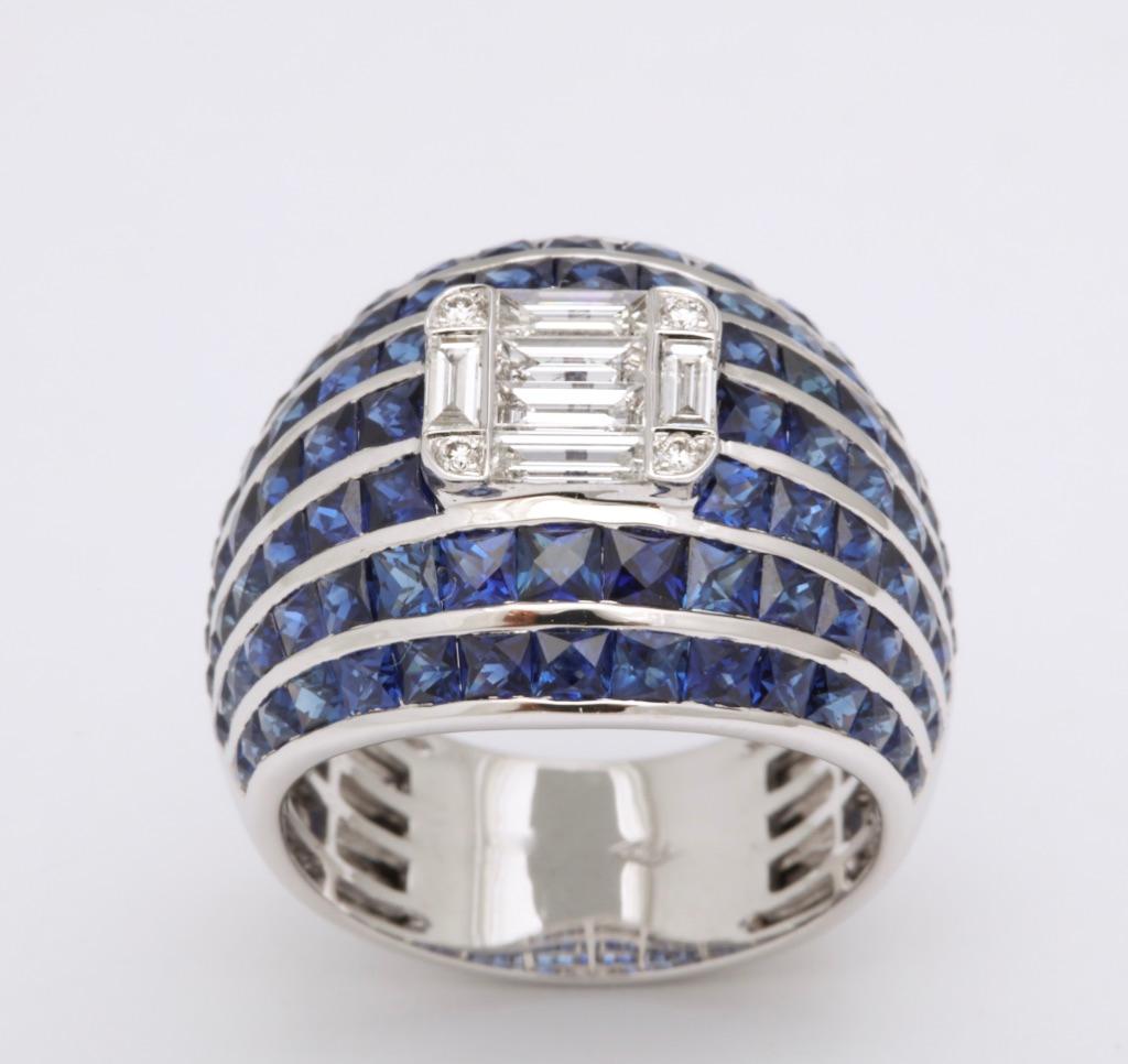 Royal blue French cut sapphires are channel set in this bombé ring, featuring a cushion shape central formation of baguette and round diamonds.  This design epitomizes the term 