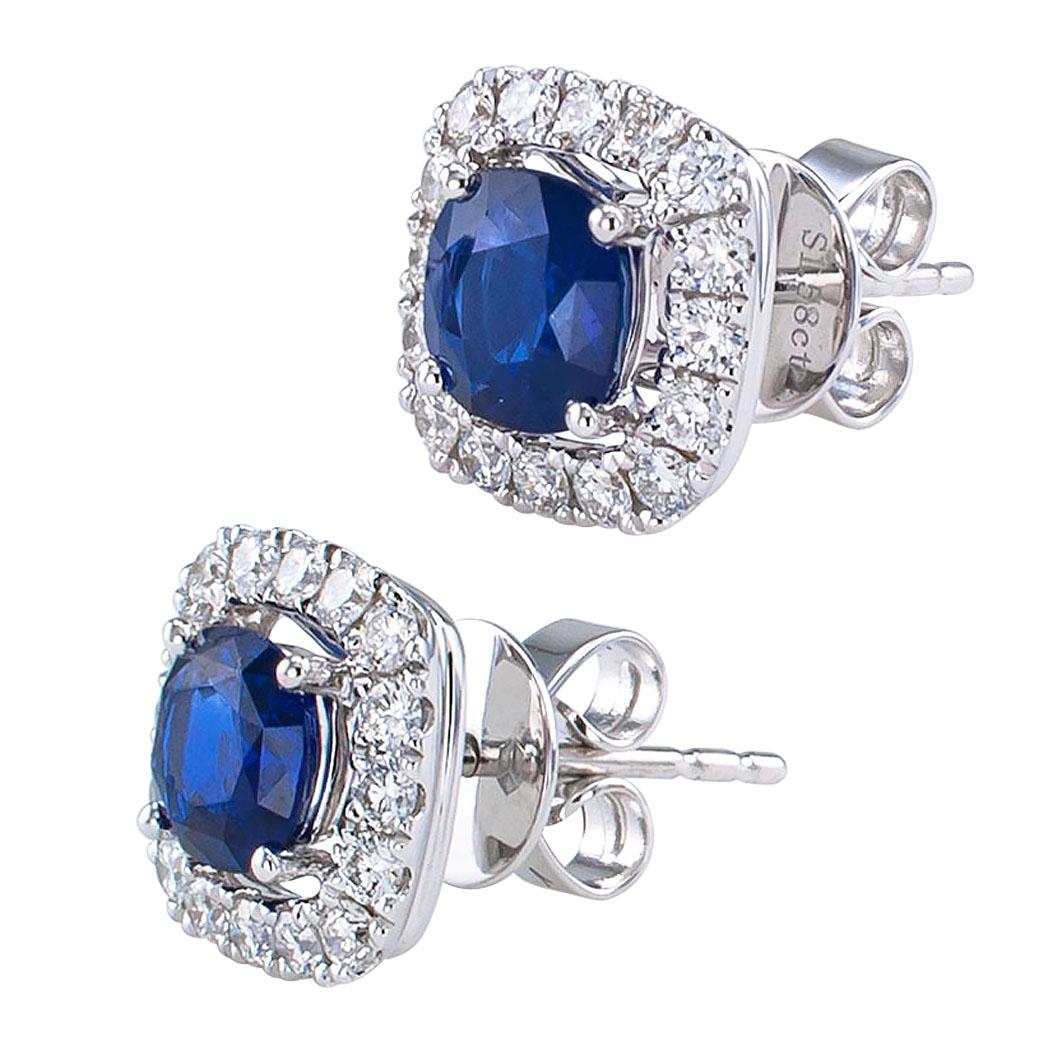 Sapphire and diamond white gold stud earrings. Showcasing a pair of cushion-shaped blue sapphires weighing approximately 1.58 carats, within a conforming border of round brilliant-cut diamonds all together totaling approximately 0.53 carat,