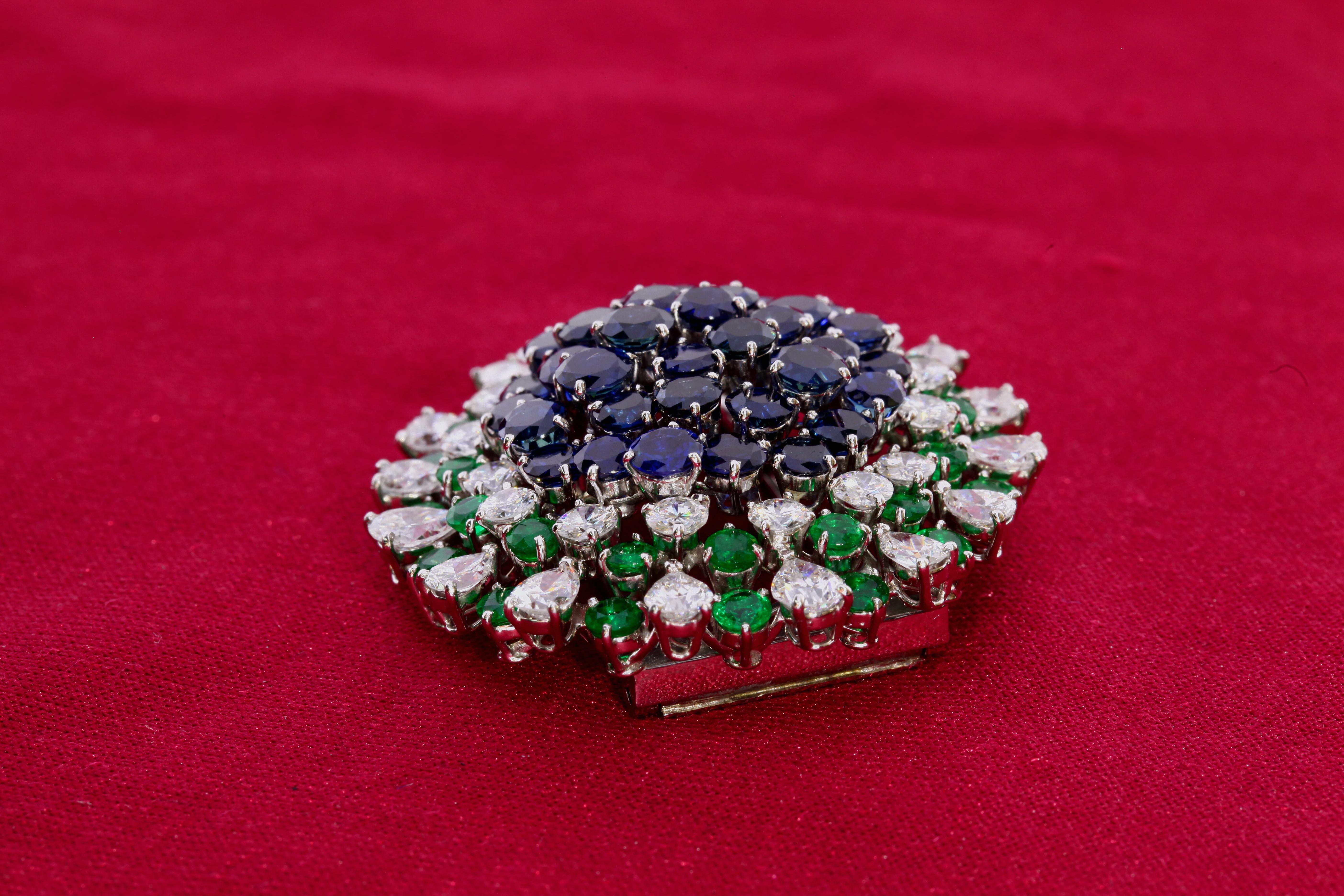 This brooch containing 35 sapphires, 32 emeralds, and 32 diamonds in a flower design. The brooch measure approximately 42mm in diameter. 