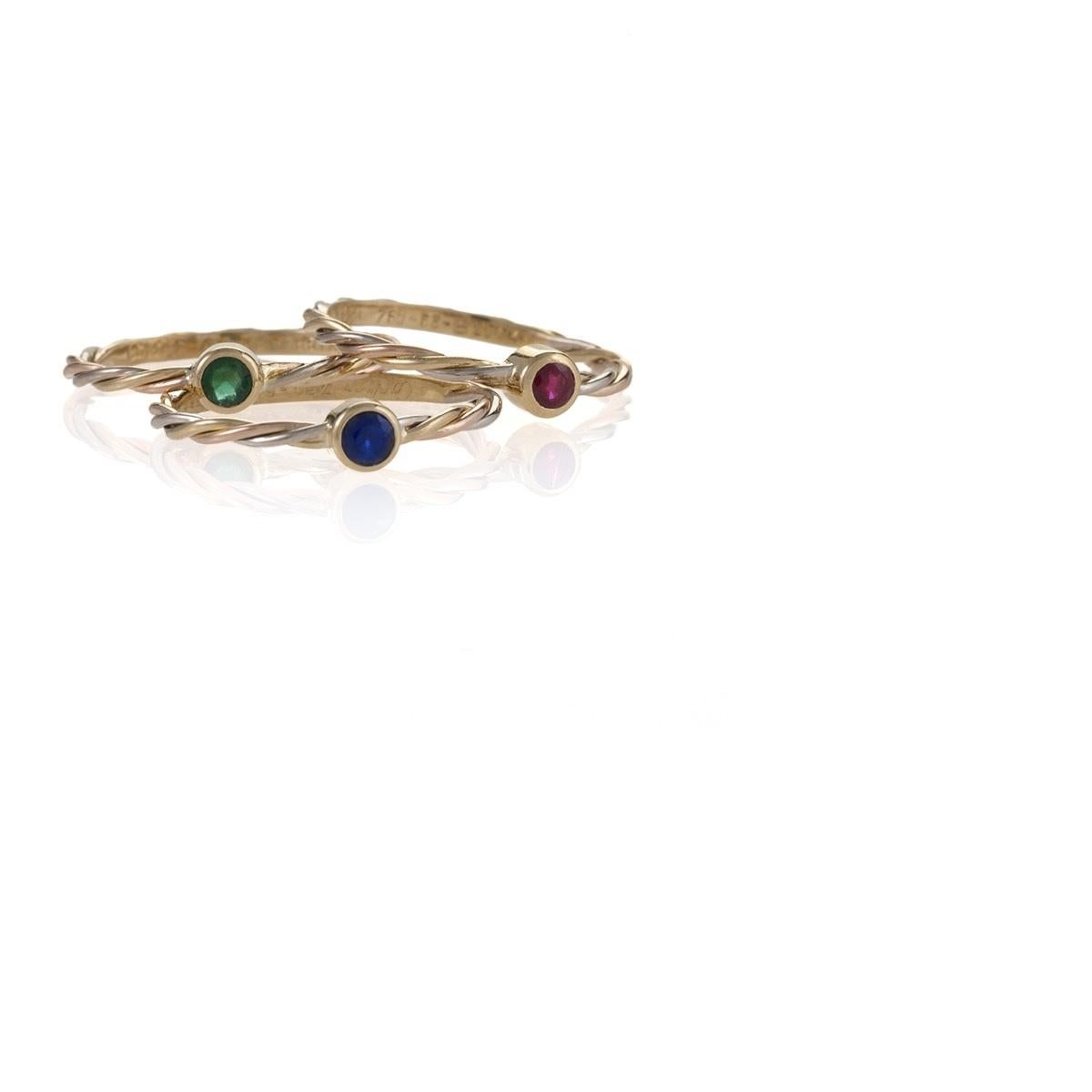 A set of rings with sapphire, emerald and ruby by Cartier. Each of the three stackable rings with twisted bands features a center stone. The gemstones are approximately .12 carat. Ring size for ruby is 6-1/4; the for sapphire and emerald rings are 