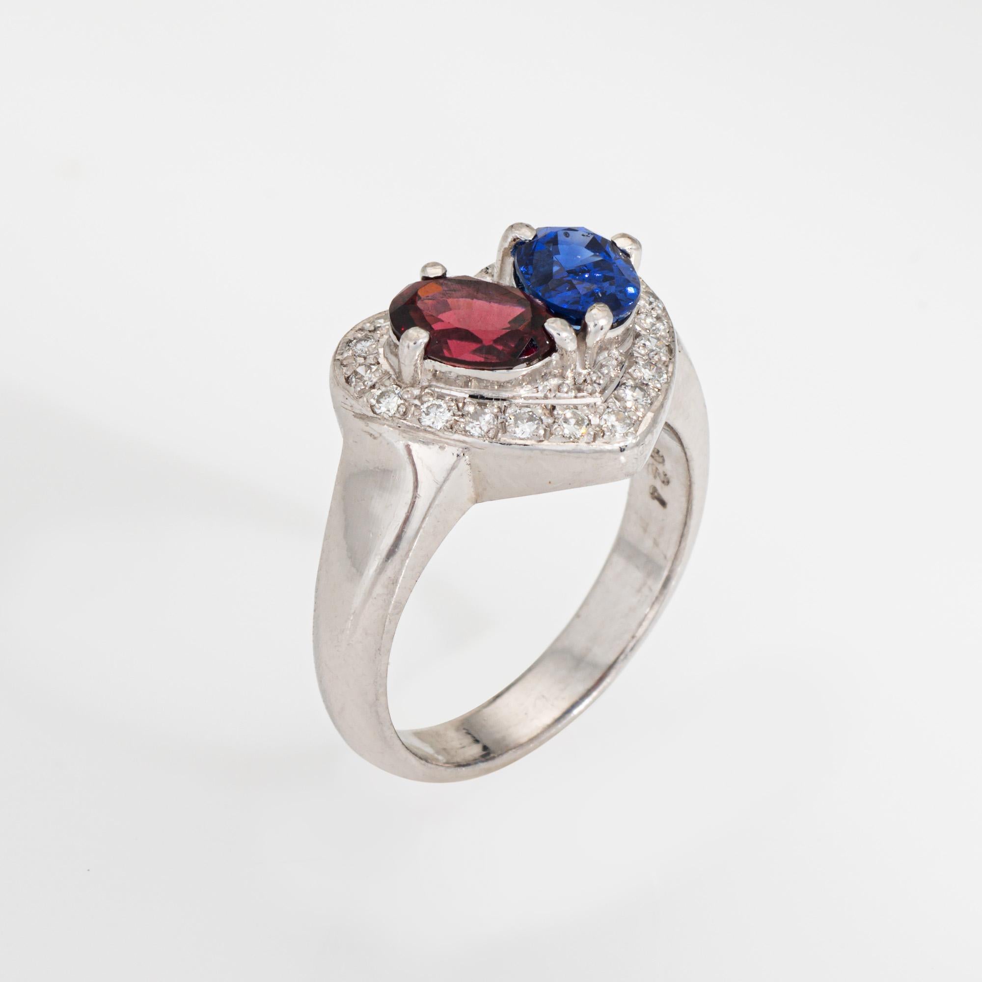Elegante anello a cuore con zaffiro e granato realizzato in platino 900. 

Lo zaffiro blu è stimato in 1 carato e il granato in 1 carato. Il totale dei diamanti è stimato in 0,24 carati (colore H-I e purezza SI1-I1).  

Questo romantico anello mette