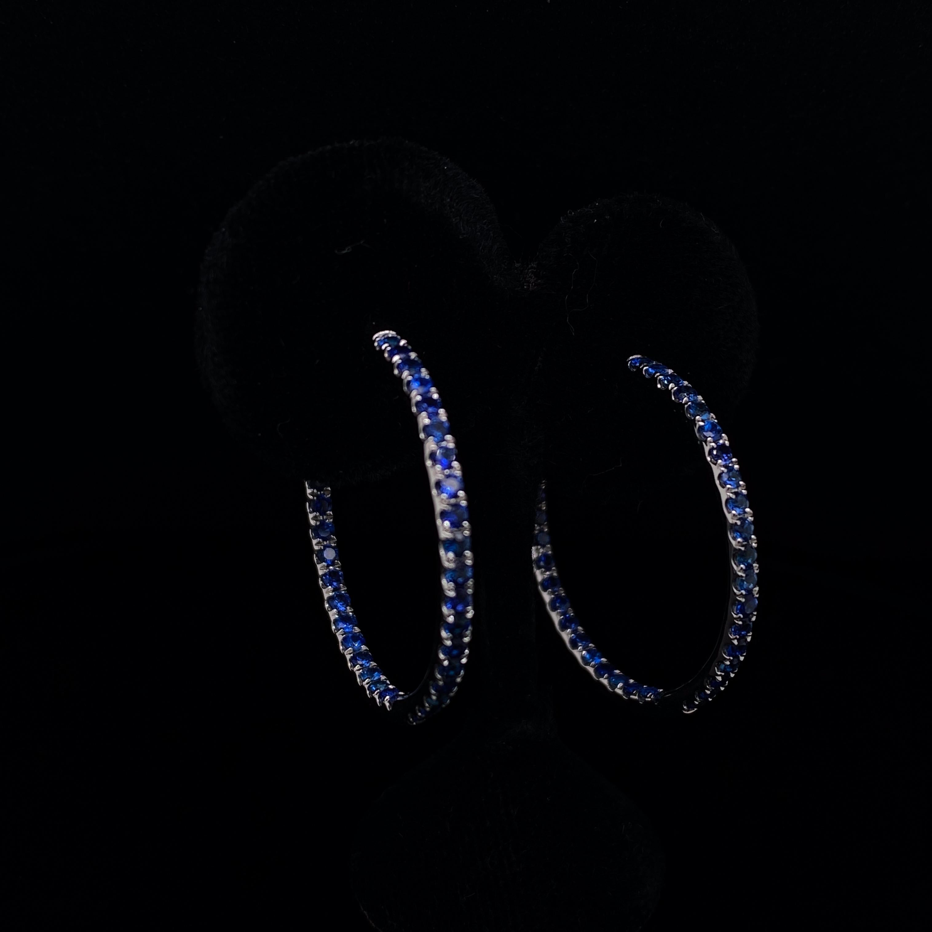 A pair of sapphire hoop earrings in 18 karat white gold.

With rich deep blue round cut sapphires claw set along the outer curve and intricately set to the inner reverse hoop of each earring, a flash of lively blue can be seen from every angle on