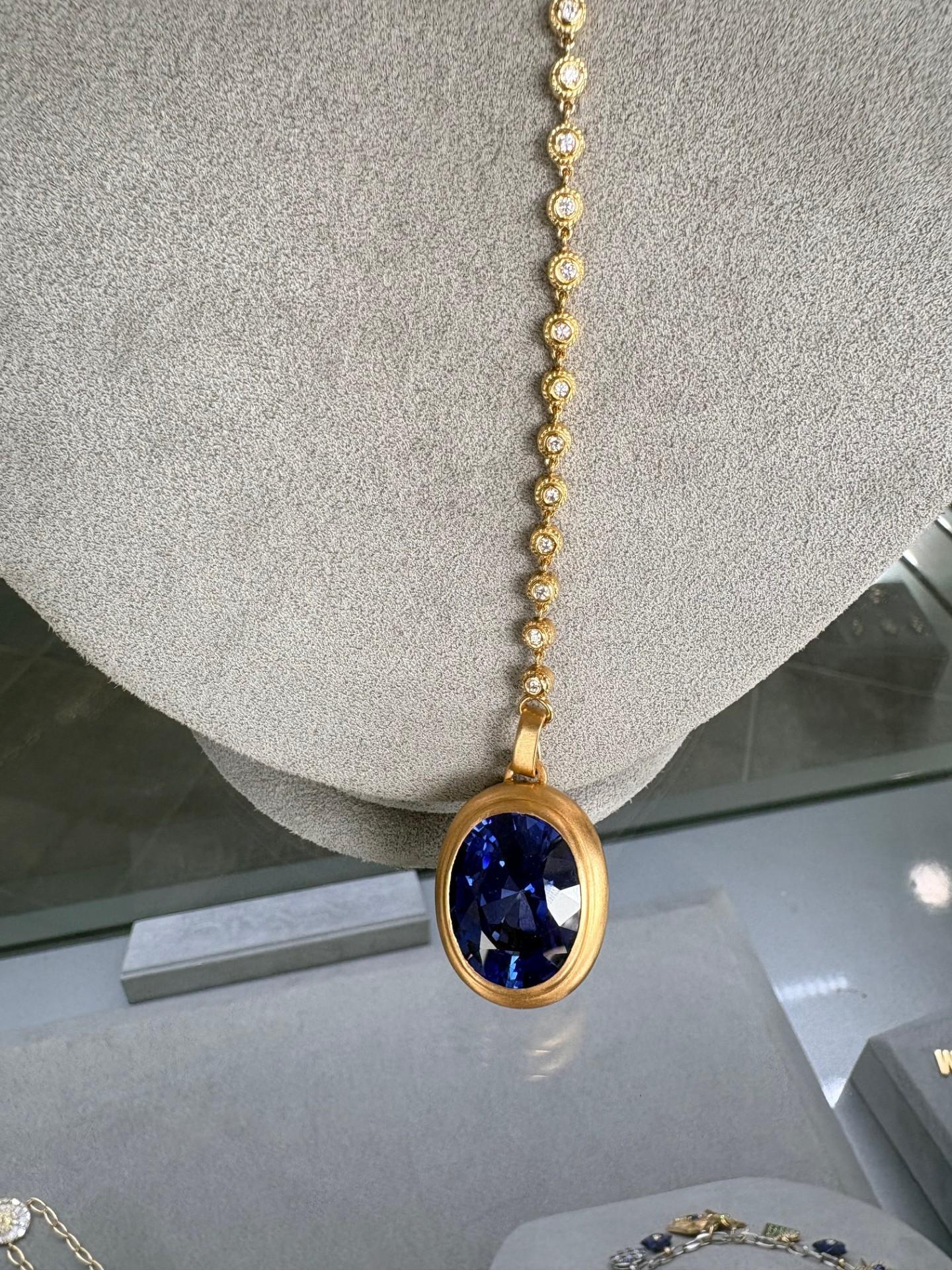 Ce pendentif remarquable est une véritable déclaration d'élégance et d'artisanat moderne. Conçue par des experts en or jaune 18 carats, elle présente une lunette satinée qui met en valeur la beauté de sa pièce maîtresse, un saphir ovale de 35,97