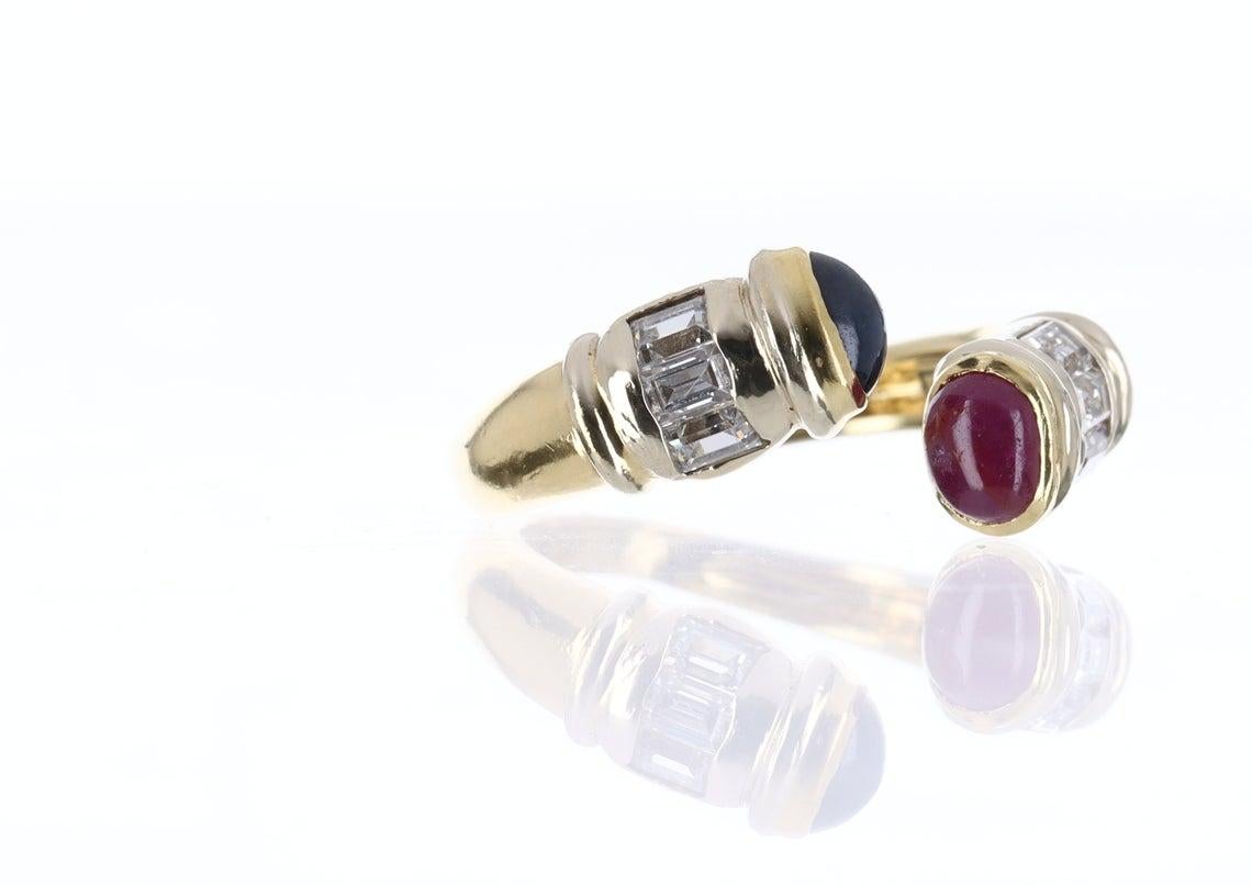 Elegantly displayed is a dual sapphire and ruby gemstone and diamond ring. Expertly handcrafted in high-quality 18k yellow gold this ring features dueling ruby and sapphire cabochons. Uniquely placed on the ends of each side of the ring the precious