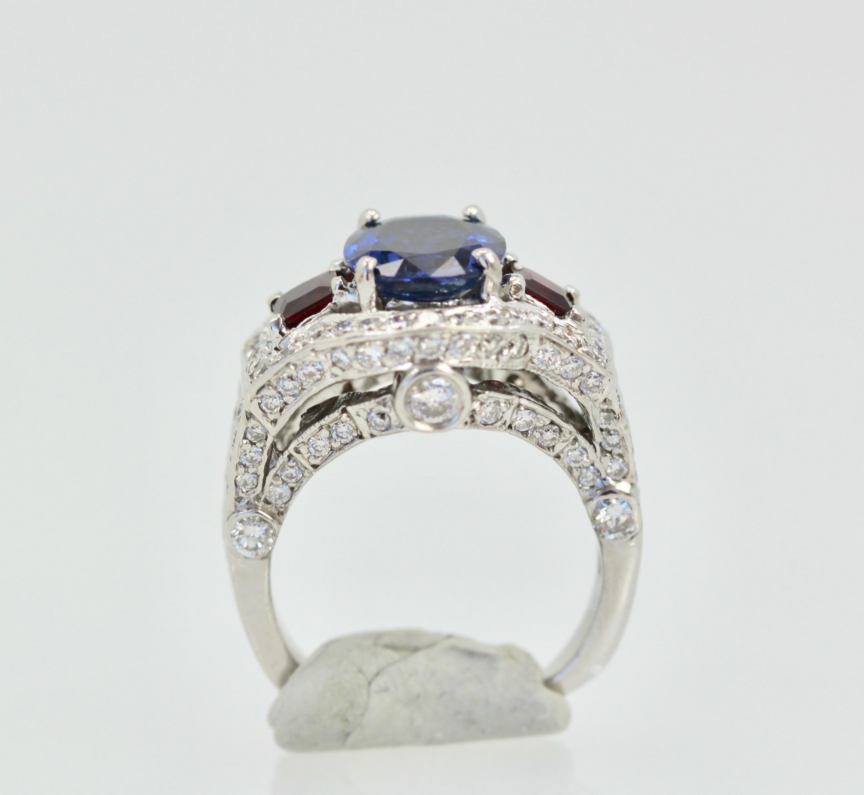 This lovely Sapphire Ruby Diamond Ring is set in 14K White Gold.  It features a Oval cut Sapphire weighing in at 2.67 Carats, flanked by 2 Rubys square cut and weighing 0.70 carats and White Diamonds, F-G, VS weighting in at 2.50 Carats.  Set in a