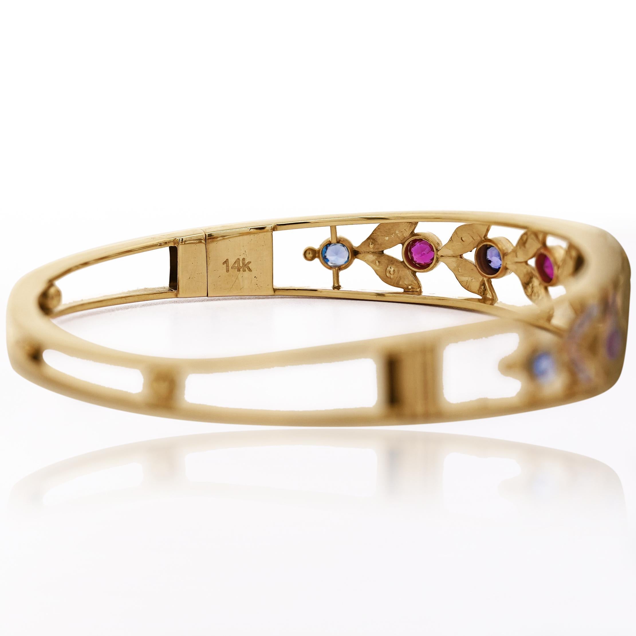 Natural sapphires, rubies, and seed pearls prong set in a 14K yellow gold openwork bangle bracelet in Art Nouveau style. Measures 8.1 inches in circumference. Not adjustable.

Details:
Item Type: Bangle Bracelet
Metal: 14K Yellow Gold (polished,