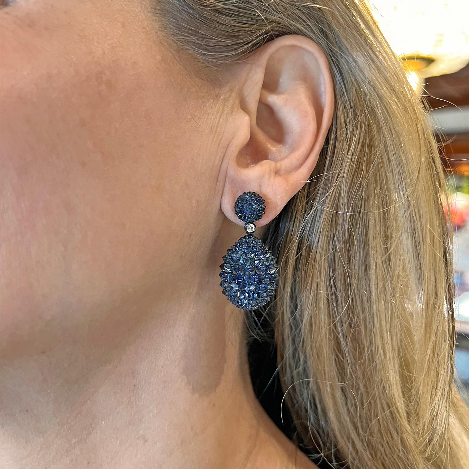 Sapphire pendant earrings, covered in reverse-set sapphires with bezel-set round brilliant-cut diamond at center.  Handmade in blue oxidized 18k gold and measuring approximately 1.5
