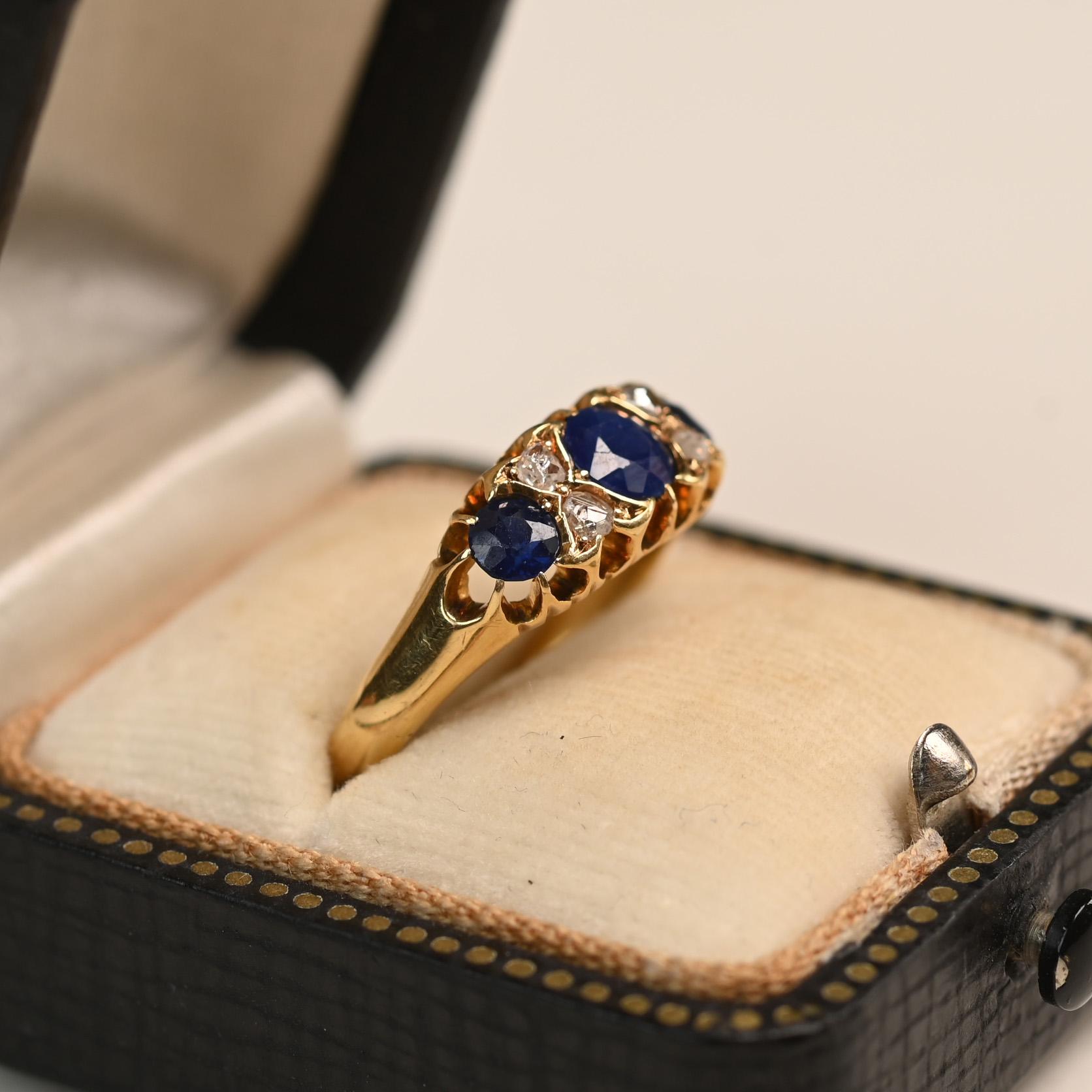 Ein fesselnder englischer Dreisteinring aus dem viktorianischen Zeitalter mit drei lebhaften, in Zacken gefassten Saphiren. Zwischen jedem Saphir ruht ein funkelnder runder Diamant, der elegant in Zacken gefasst und mit zarten Golddetails in