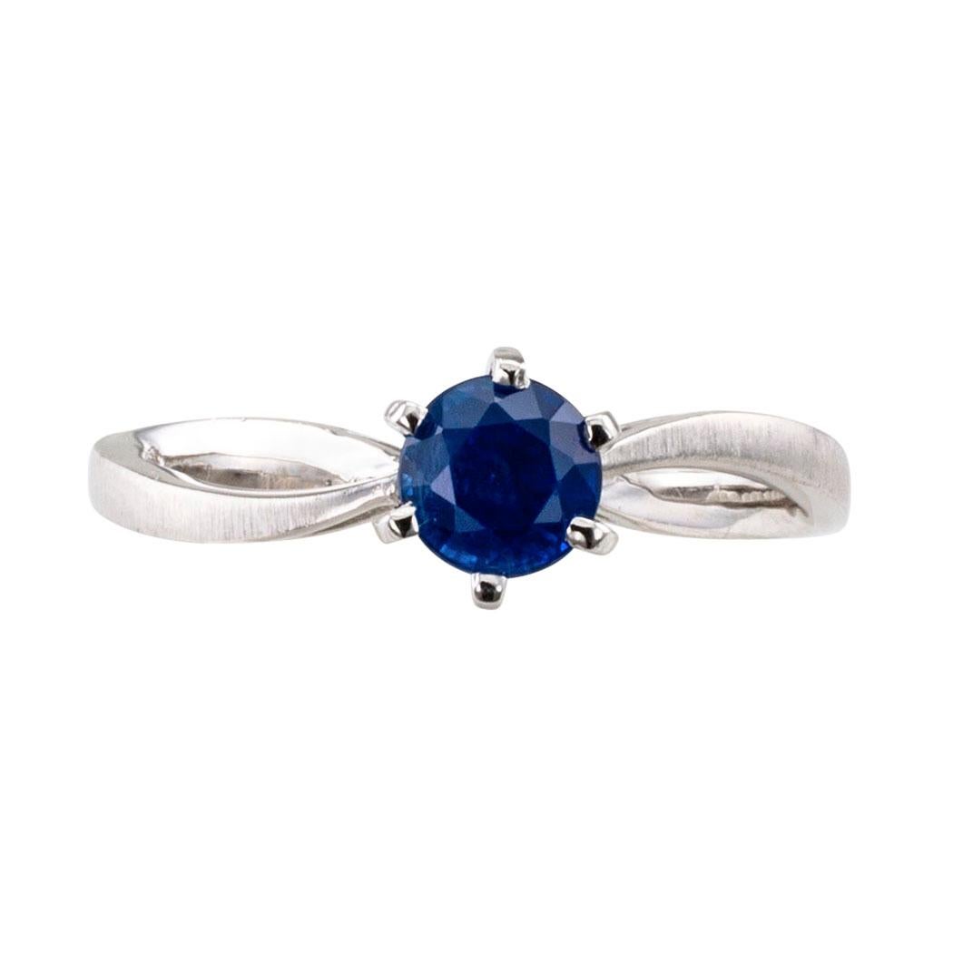 Sapphire and white gold solitaire engagement ring. The petite 14-karat white gold solitaire ring centers upon a round, blue sapphire weighing approximately 0.68 carat, on a simple six-prong setting between curved and split shoulders contrasted with