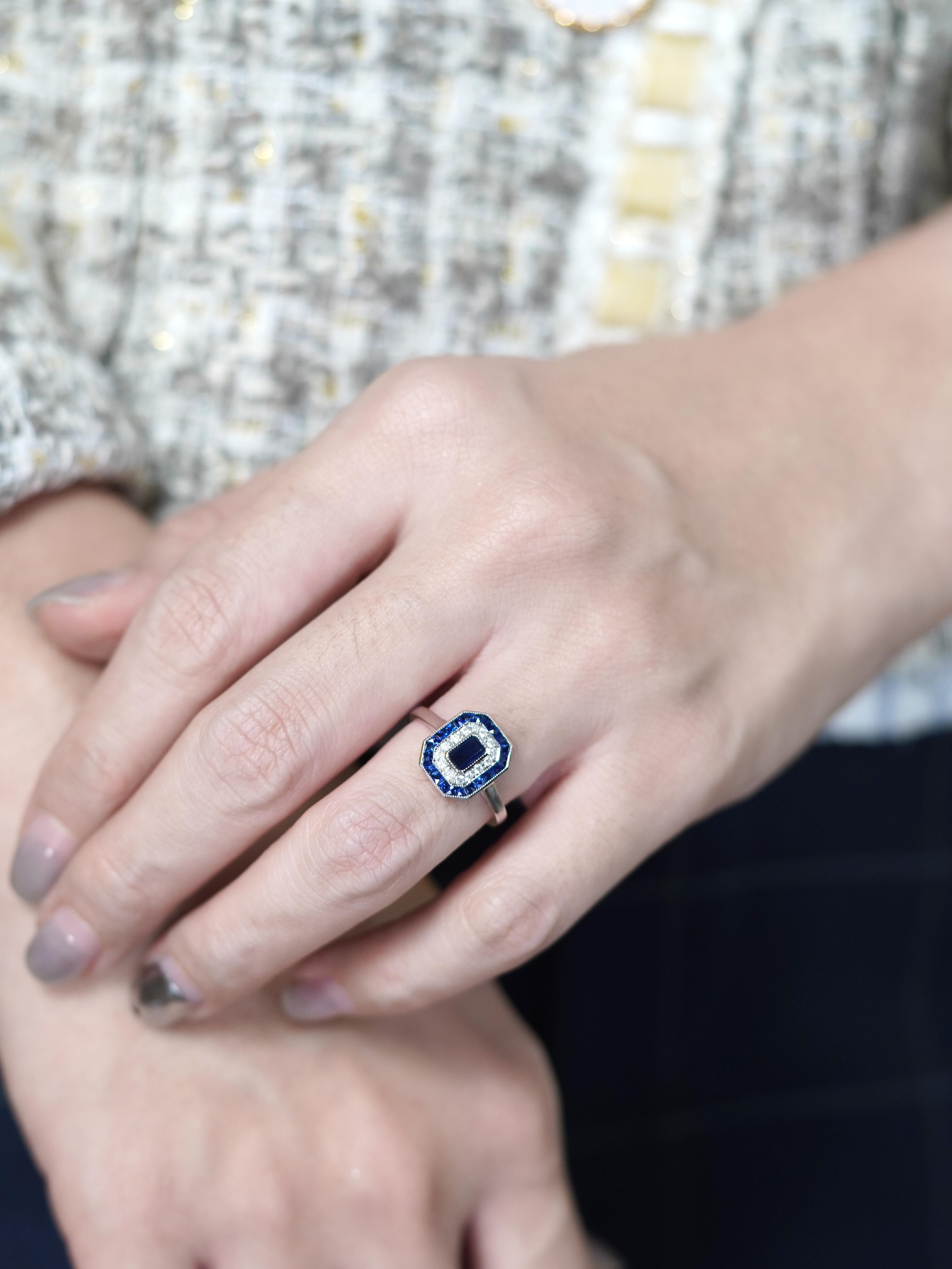 Immerse yourself in timeless elegance with this captivating Art Deco-style ring, crafted in luminous 14K white gold. At its heart lies a deep, velvety sapphire, surrounded by a halo of shimmering diamonds that dance with every glance. Framed by