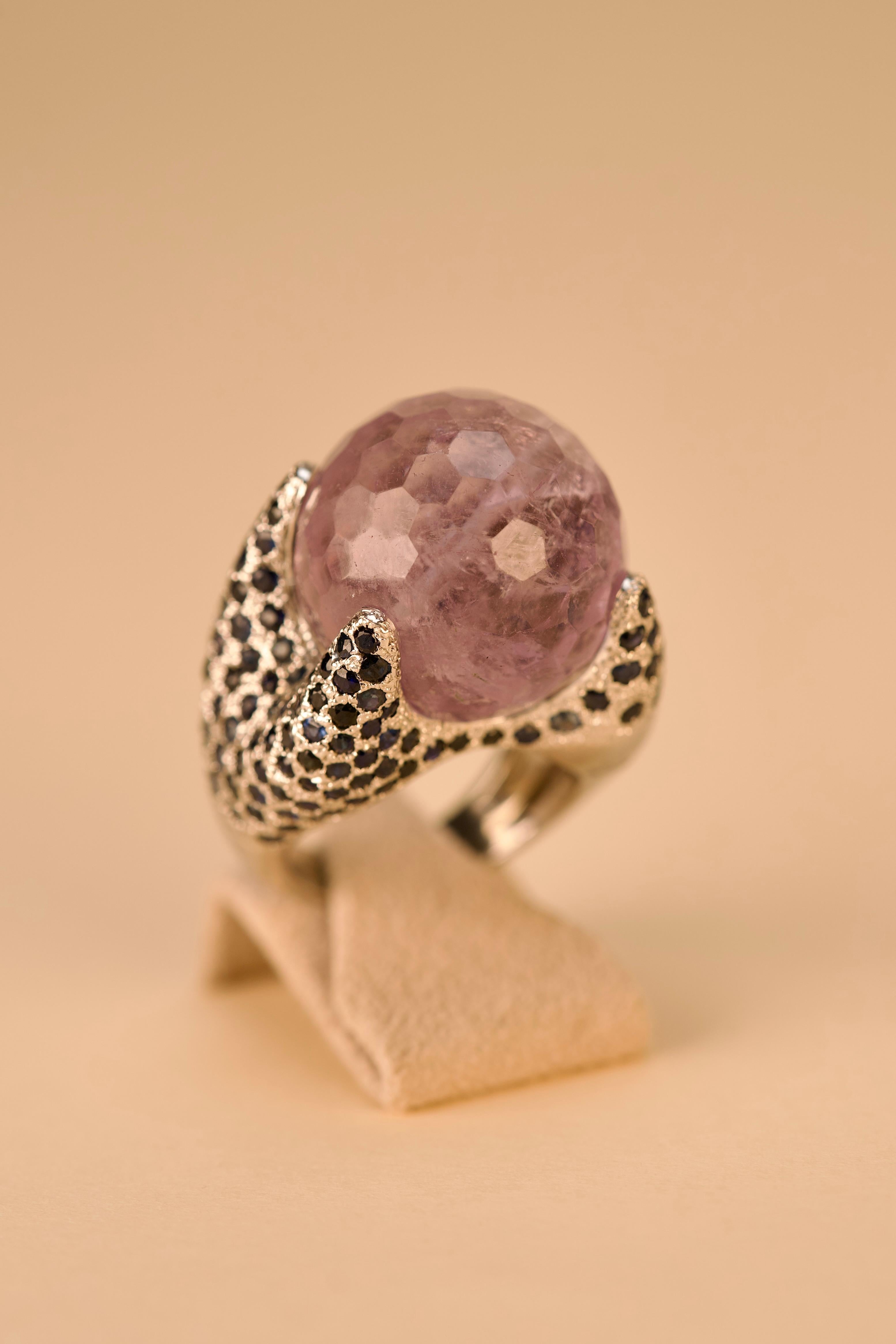 18kt – 750‰ white gold ring with 1 faceted spherical amethyst mea suring20.0mm diameter in the center, surrounded on both sides by blue sapphires. Polished finish


