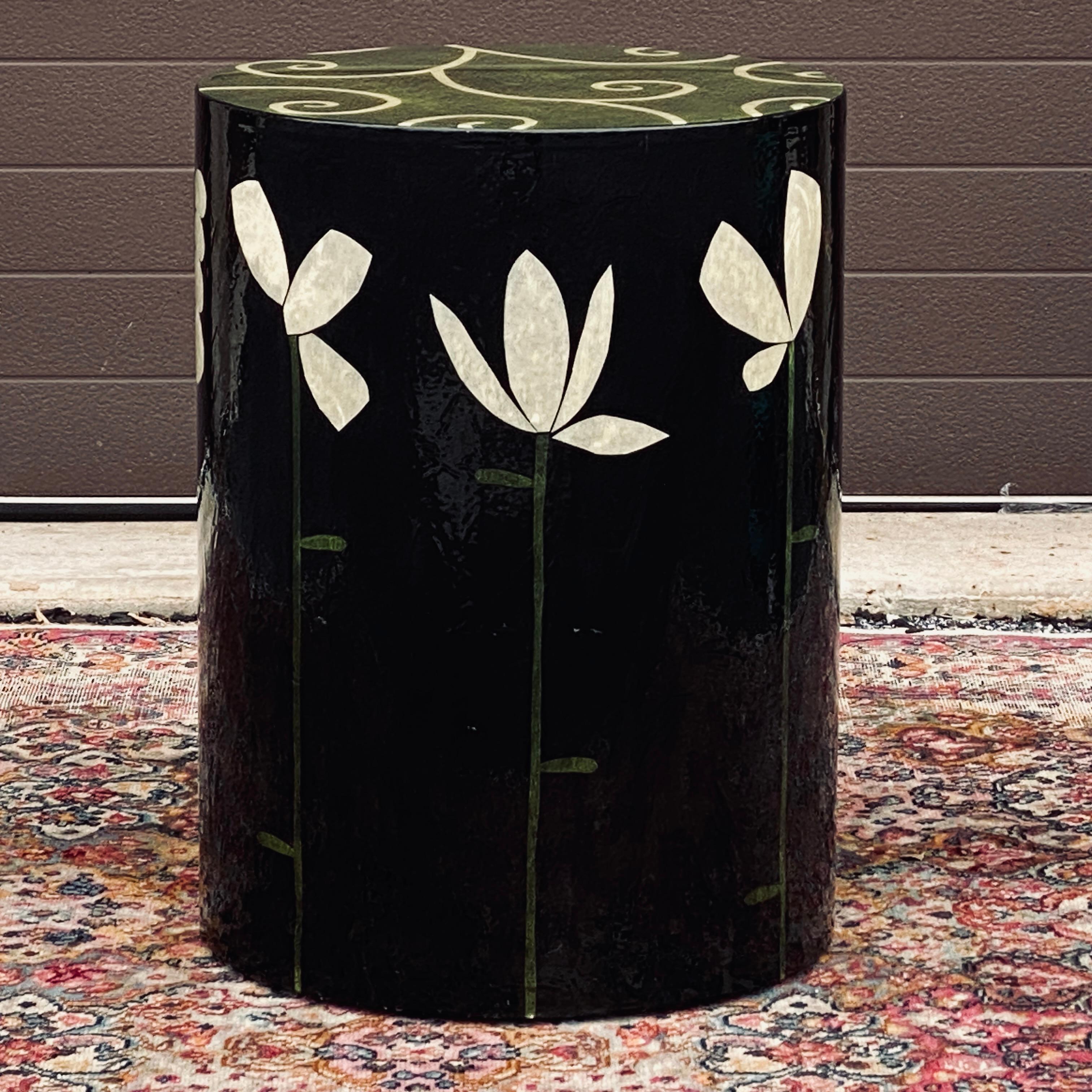 Whimsical floral folk art cylindrical side table by Sara Moore. Decorated around the circumference with green and white stems over a charcoal background. Can be moved around the room easily on the hidden casters. 