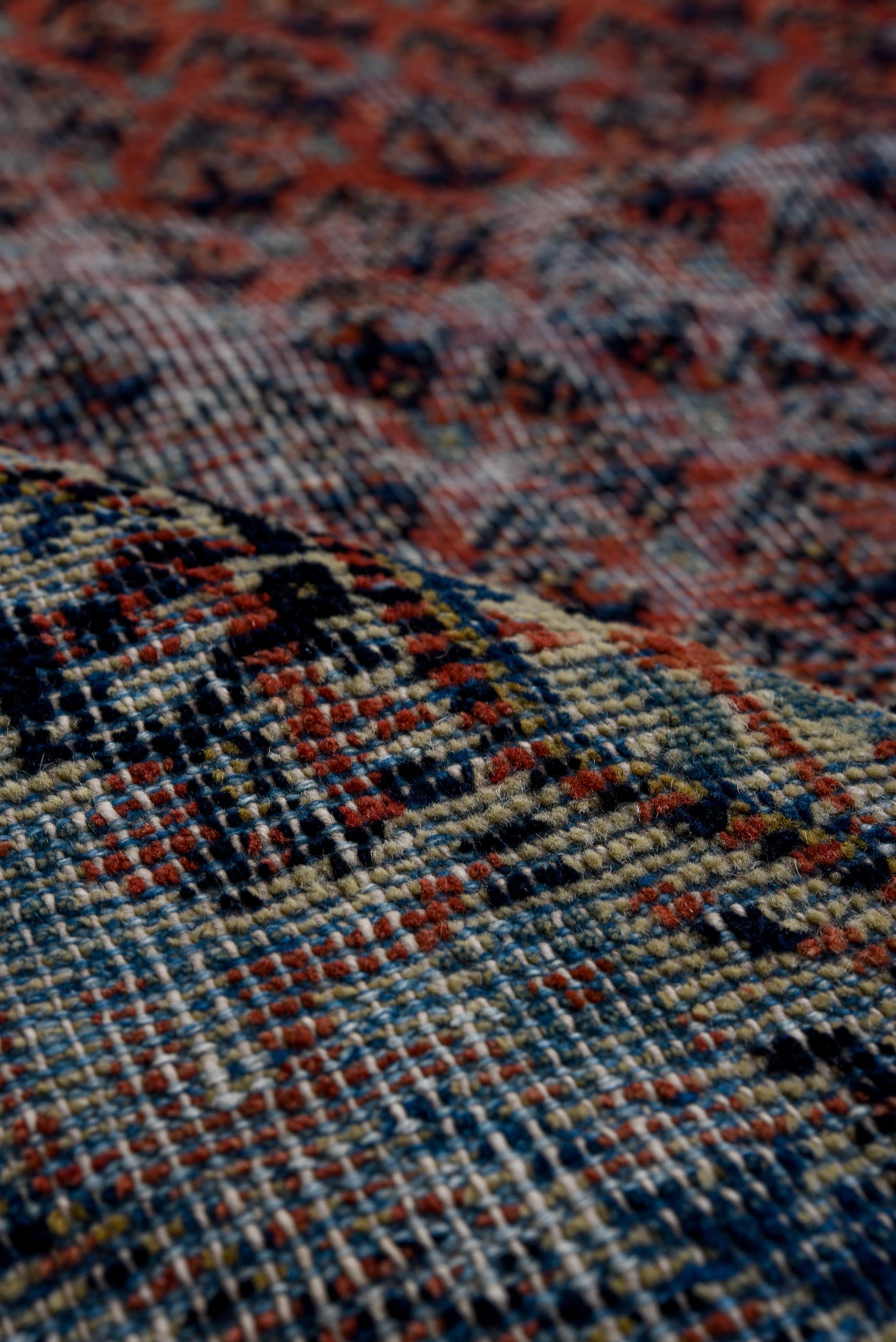 Classic boteh latticework in madder red over an oxidized indigo field, softened by visible wear and abrash for a vintage, distressed feel. Ivory border details frame the design with delicate floral scrolls and angular corner motifs. A mellow tribal