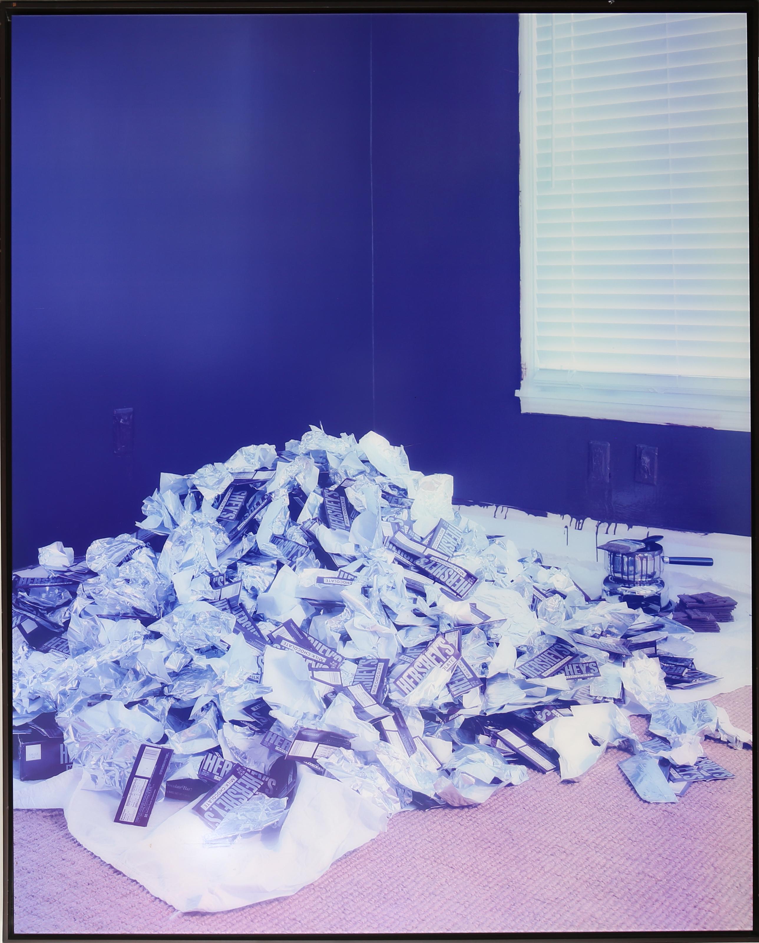 “Obsessiveness” is a chromogenic print by artist Sarah Hobbs (b.1970), dated 2003, edition 1/5. The photograph depicts a large pile of crumpled Hershey’s chocolate bar wrappers and packaging accumulated on a pink carpet against deep blue walls, with