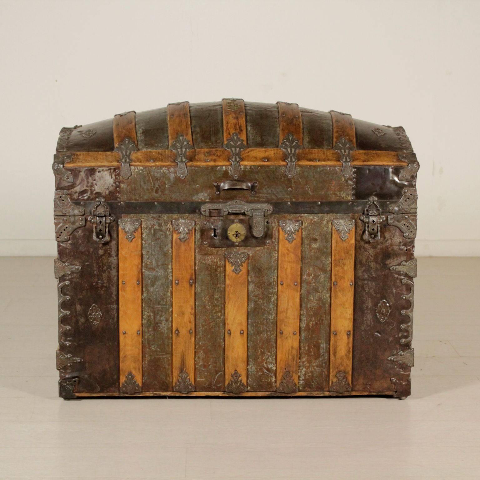 A trunk, barrel top named Saratoga. Wood structure covered with metal. Diagonal slats on the sides, front and back. Typical rounded top. Elegant clamps made of chiselled metal on the corners and the links. Lock with double chiselled pivot (the left