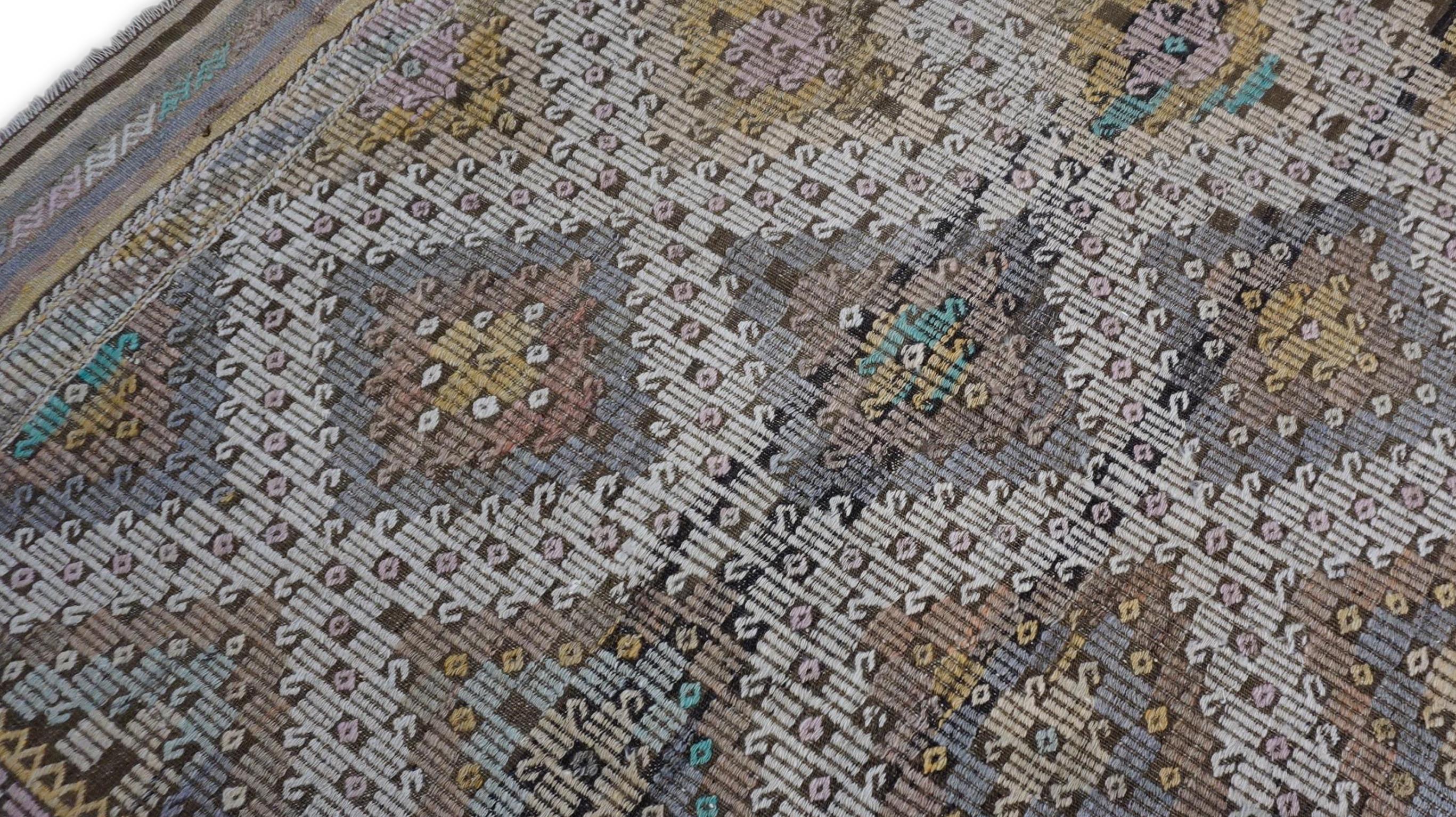 Dieser exquisite Kelim aus Vintage-Wolle zeigt eine faszinierende Anordnung geometrischer Medaillons, die in einem strukturierten, sich wiederholenden Muster angeordnet sind. Das zentrale Feld ist mit aufwendig gewebten Rautenmotiven verziert, die