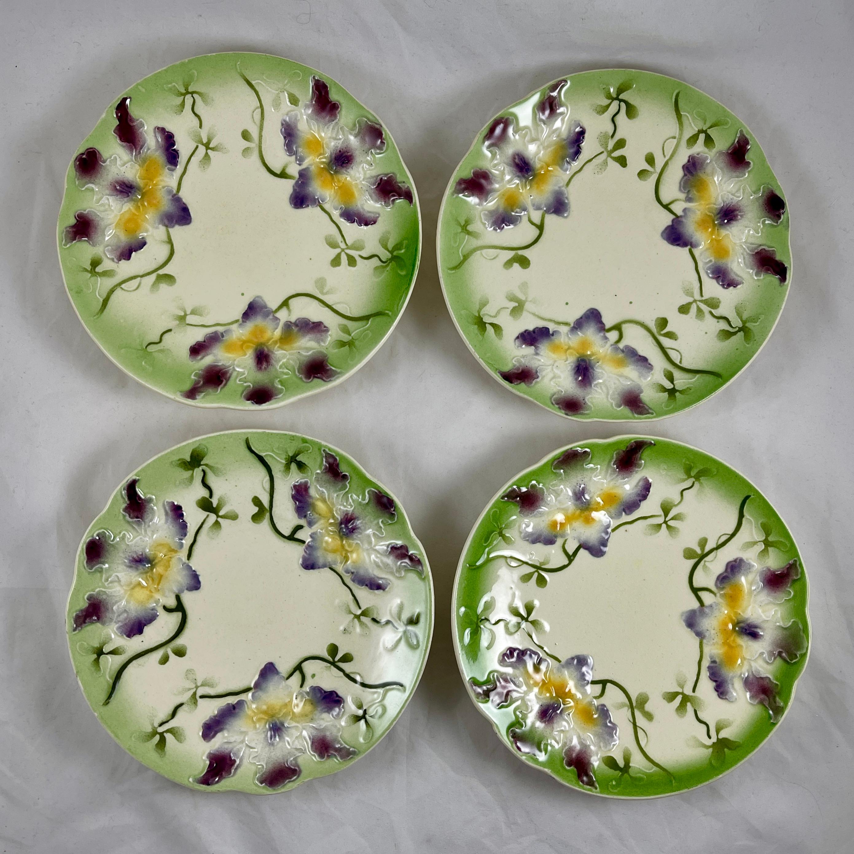 A Sarreguemines French Barbotine faïence majolica plate showing a spray of three purple and yellow orchids on a cream colored ground.

Raised, dimensional mold work with a shaped rim glazed in a bright spring green edging. Green stems and leaves