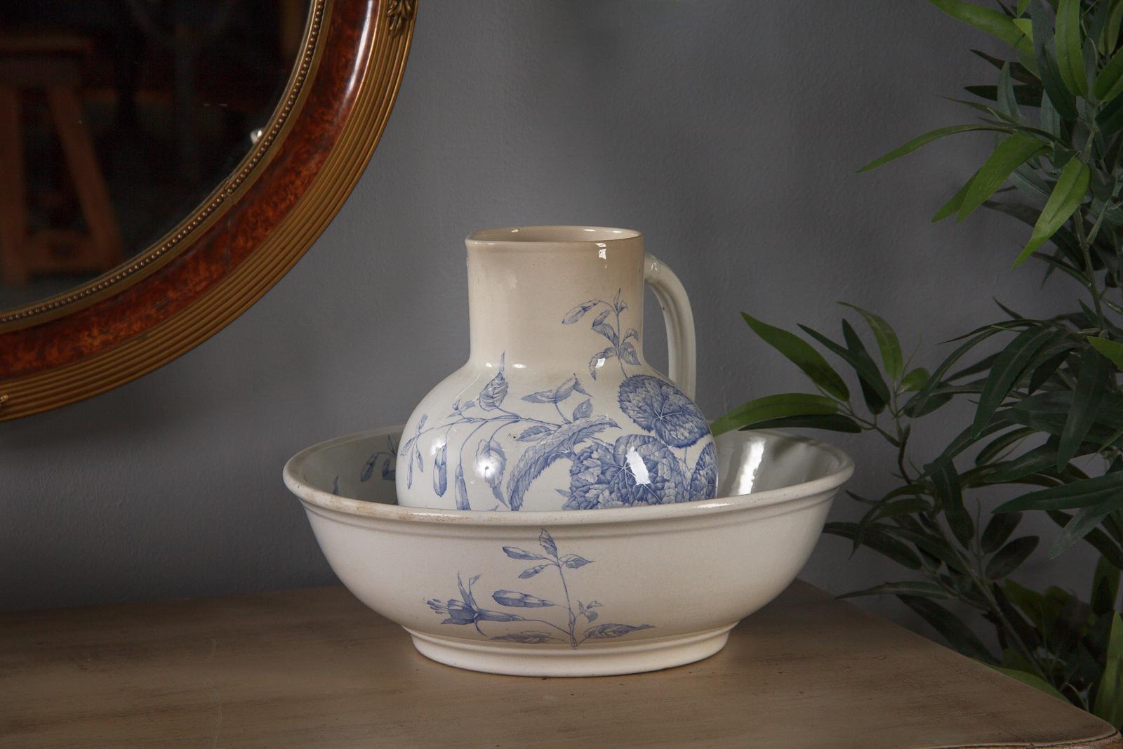 A blue and white pitcher and bowl from the Sarreguemines ceramic factory in Eastern France, circa 1920. White ceramic with indigo printed images of various flowers, detailed foliage and a single delicate butterfly. The wide bowl has foliate
