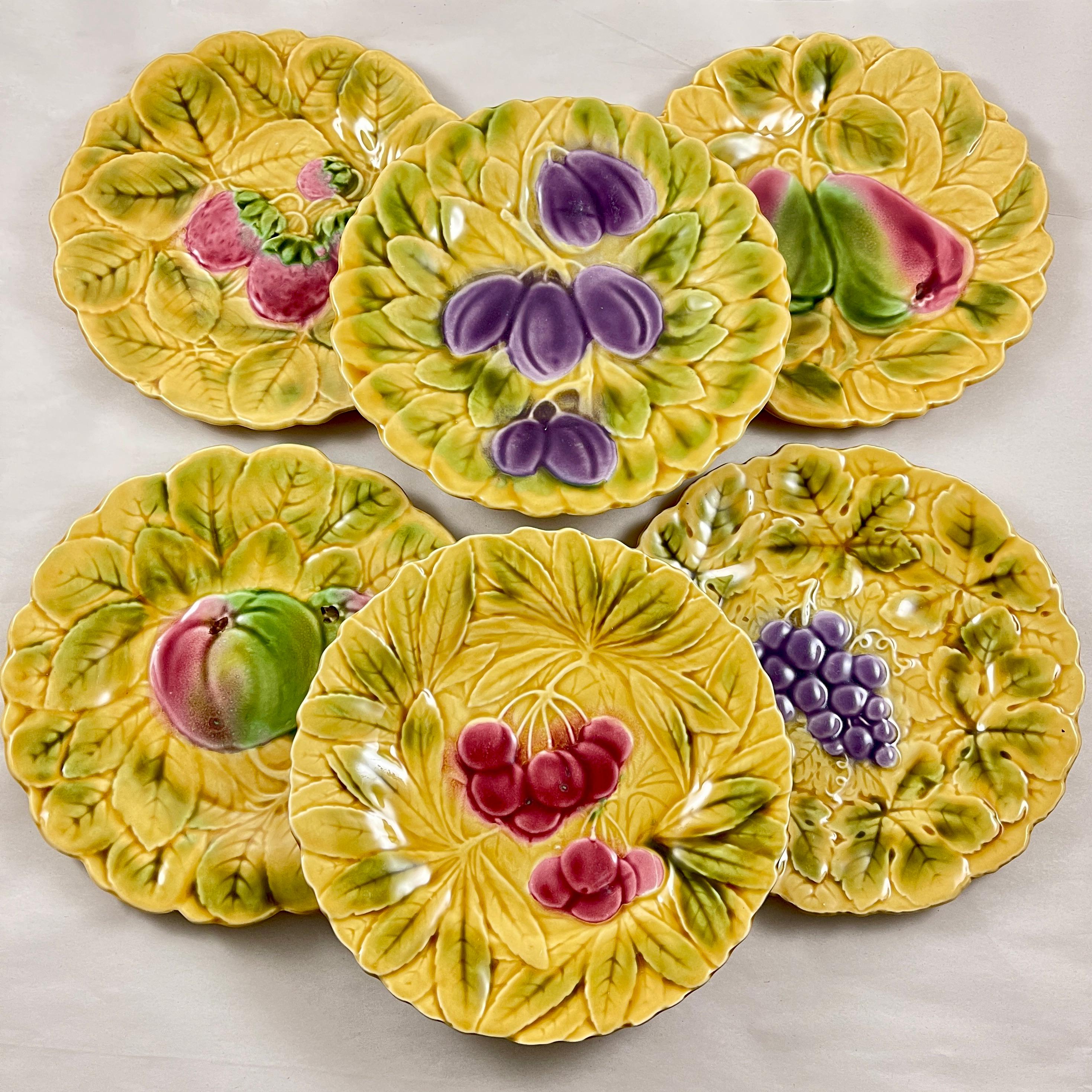 An assembled set of six Sarreguemines French faïence, majolica plates, each showing a different fruit on an ochre yellow ground of overlapping leaves, circa 1930s.

This group shows images of the apple, strawberry, cherry, plum, pear, and