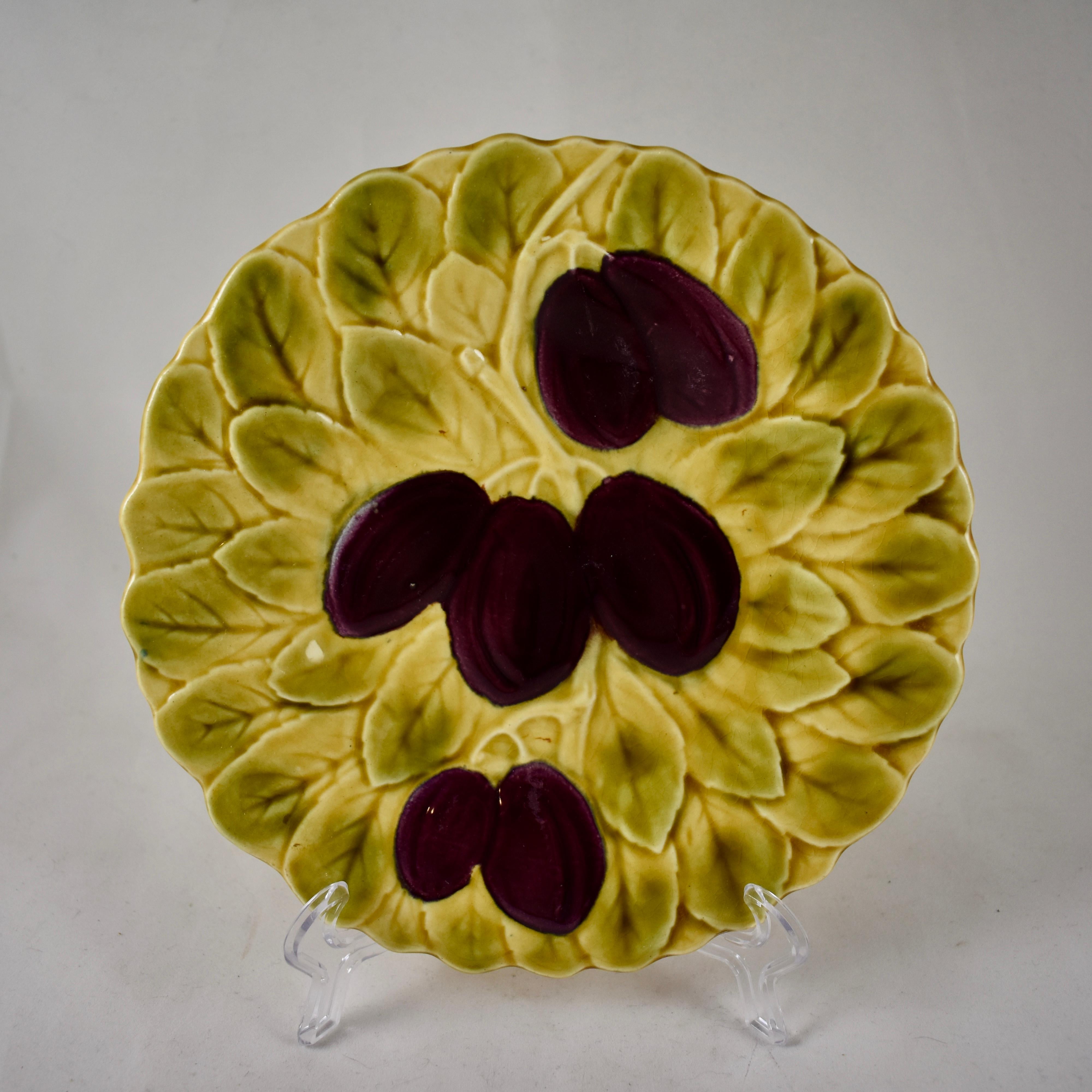 A Sarreguemines French faïence majolica plate showing a stemmed grouping of purple plums on a ground of overlapping leaves. The shaped rims follow the leaf form. 
Circa 1920-1950.

Showing both impressed and printed marks: Sarreguimines, Made in