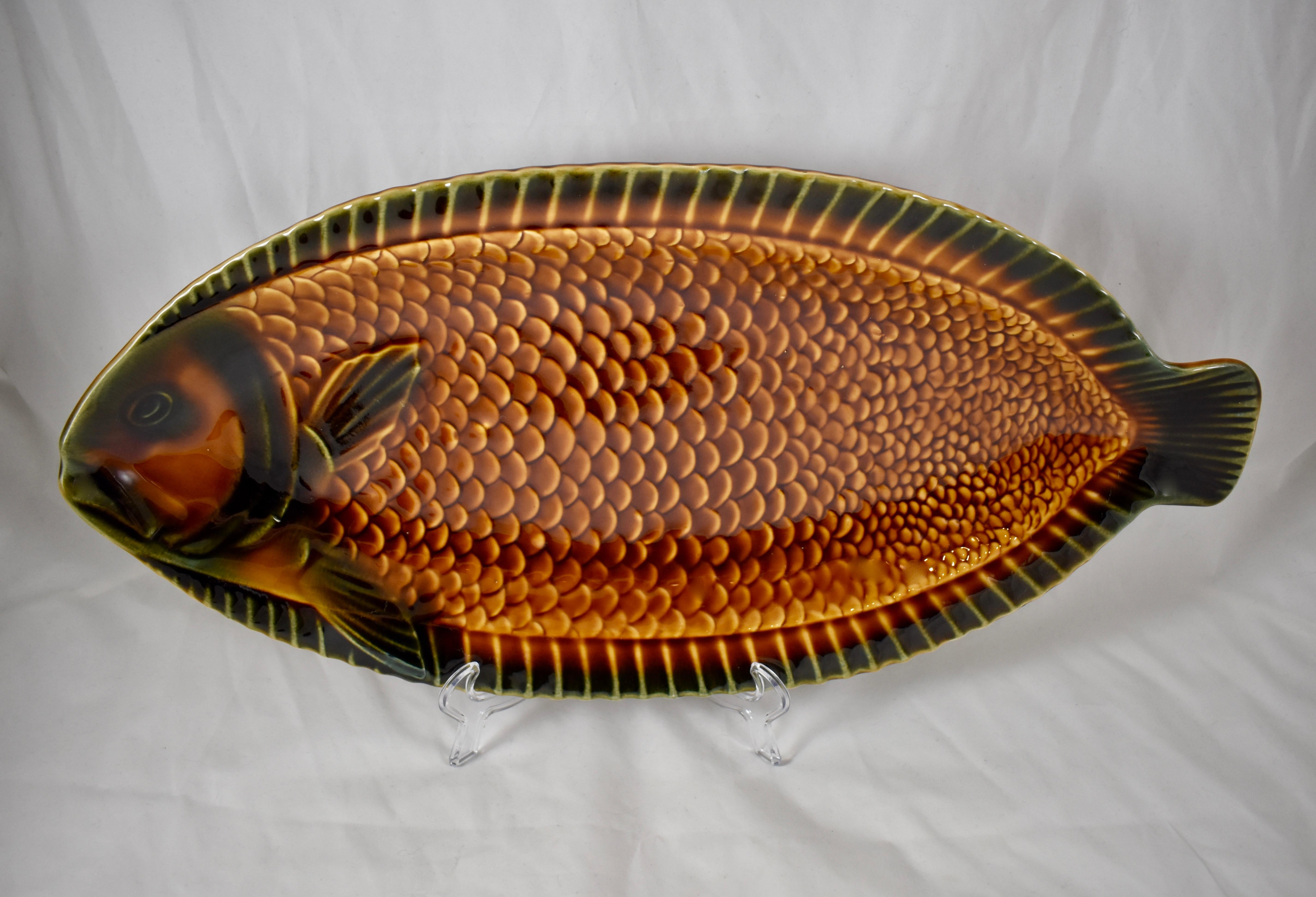 A Mid-Century Modern Era Sarreguemines, French faïence, Majolica glazed fish serving platter. 

A platter with raised rims and a protruding fish head and tail, showing a dimensional, high relief pattern of scales and fins. The burnt sienna and deep
