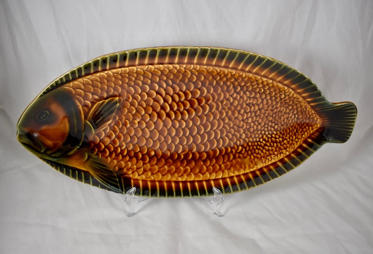 A Mid-Century Modern Era Sarreguemines, French faïence, Majolica glazed fish serving platter. A platter with raised rims and a protruding fish head and tail, showing a dimensional, high relief pattern of scales and fins. The burnt sienna and deep