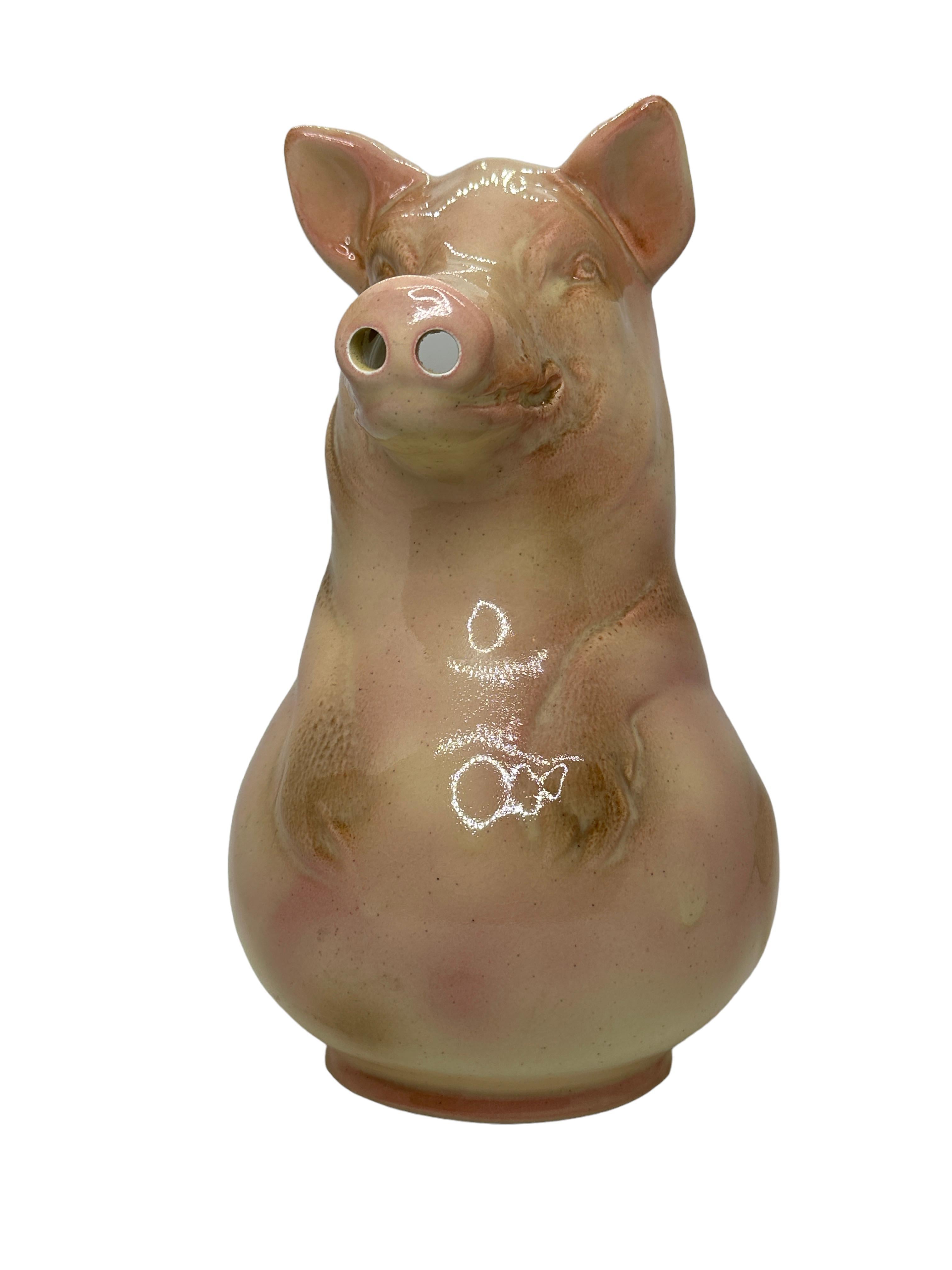 Decorate a shelf or a kitchen counter with this elegant antique barbotine pitcher. Created by Sarreguemines, France in the 1930s, the pitcher depicts a smiling pig figure hand painted in a cream palette with pink nose and ears. The water jug is in