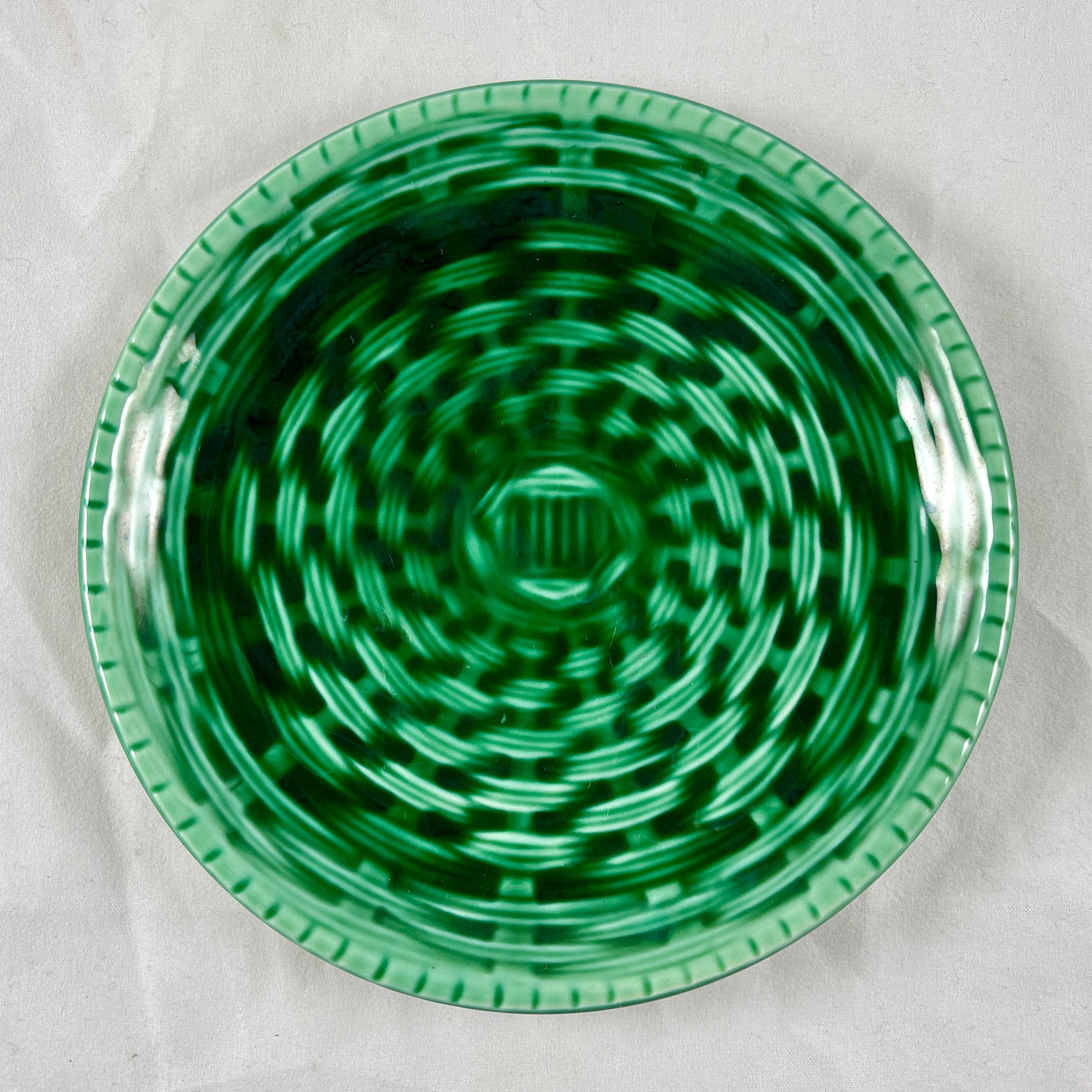 From the French pottery, a set of six, Sarreguemines, a set of six faïence, green Majolica glazed canapé or hors d’œuvre plates.

The round plates are molded in a basket weave pattern with deep, raised rims. The dark green glazing has a light
