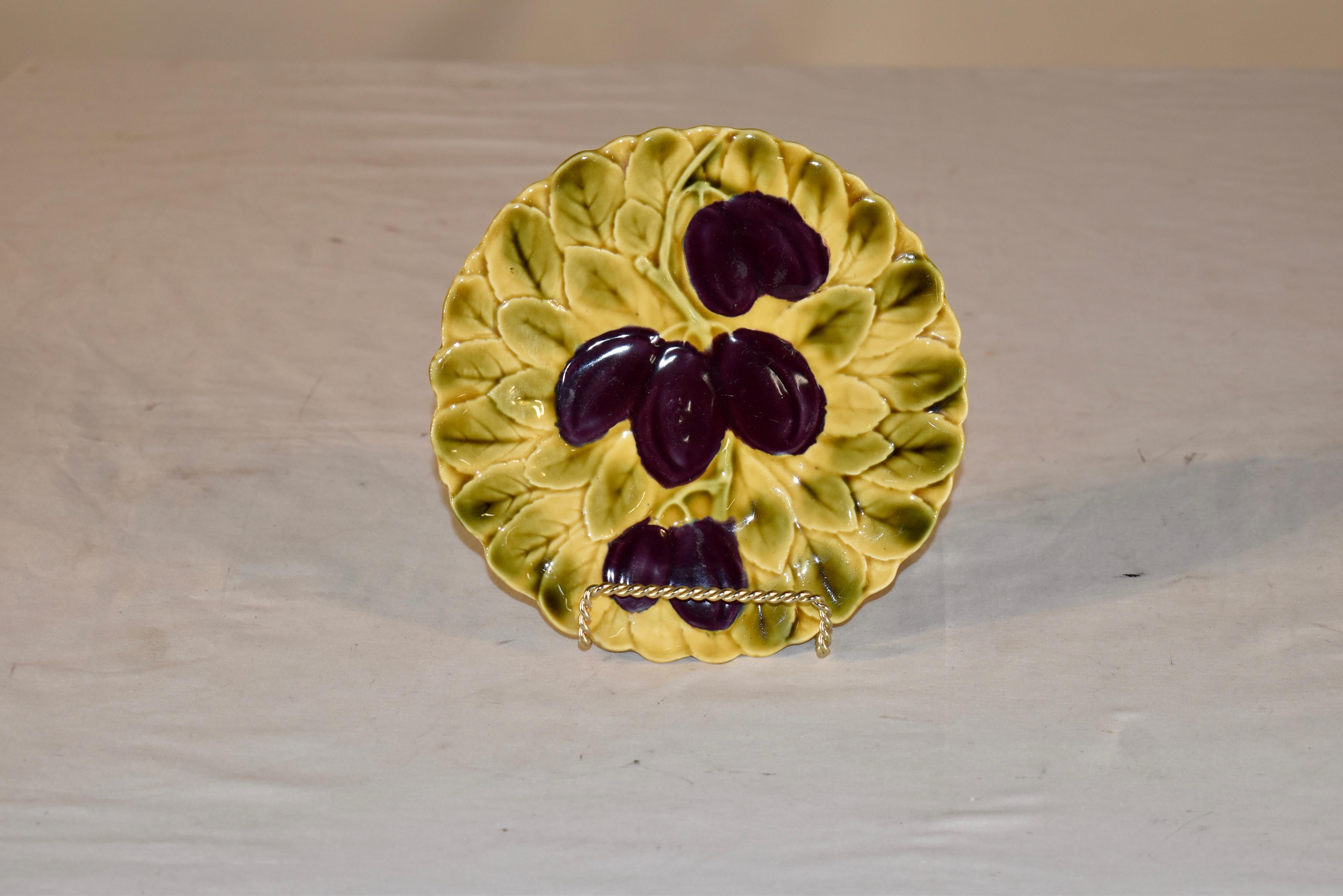 Signierter Majolikateller von Sarreguemines mit Pflaumen auf einem Bett aus Blättern in der Mitte. Das Muster ist reliefartig, was dem Design einen zusätzlichen Reichtum verleiht und das Muster und die Farben richtig zur Geltung bringt.  
Dies wird