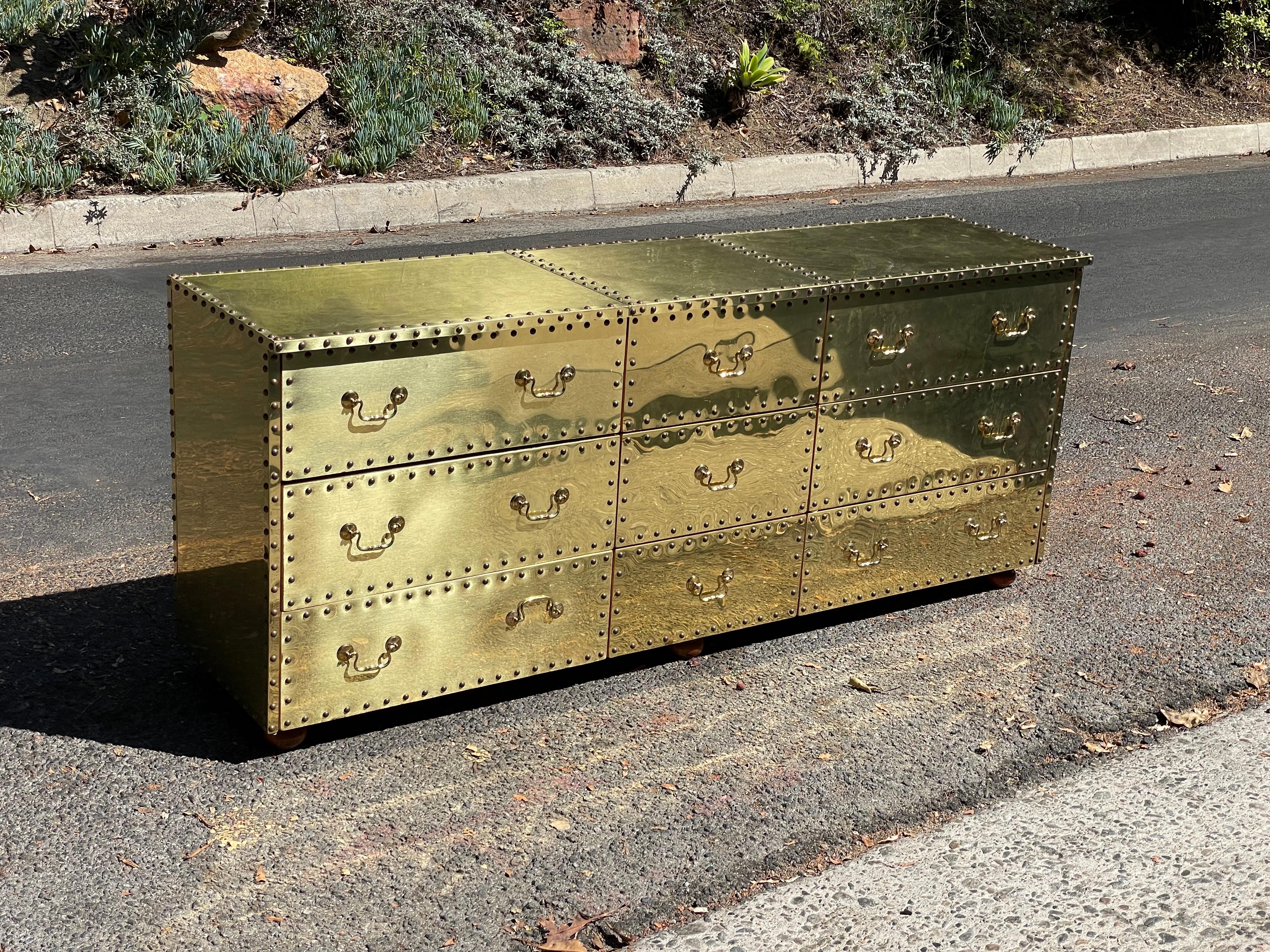 Striking mid-century brass clad nine-drawer dresser with nailhead trim by Sarreid Ltd. Circa 1970s.

Clad on three sides with solid brass sheeting, this triple dresser is one of the most sought after of the vintage Sarreid designs. It really makes a