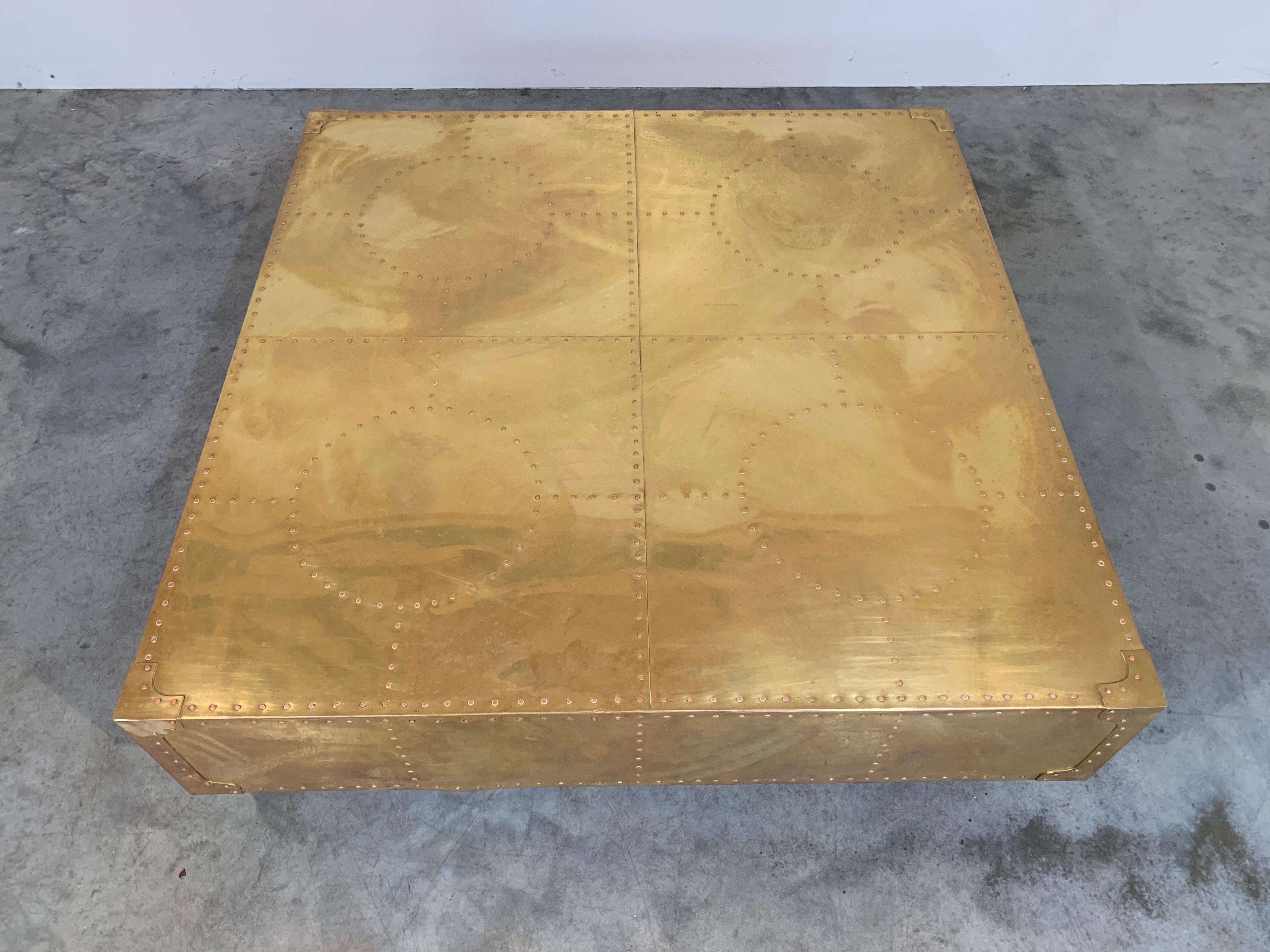 A rare coffee table form by Sarreid. Wrapped in brass having copper rivets throughout over a plinth wooden base.
 Beautiful well maintained condition throughout. We also polished it for its new home. The protective glass top is optional at no