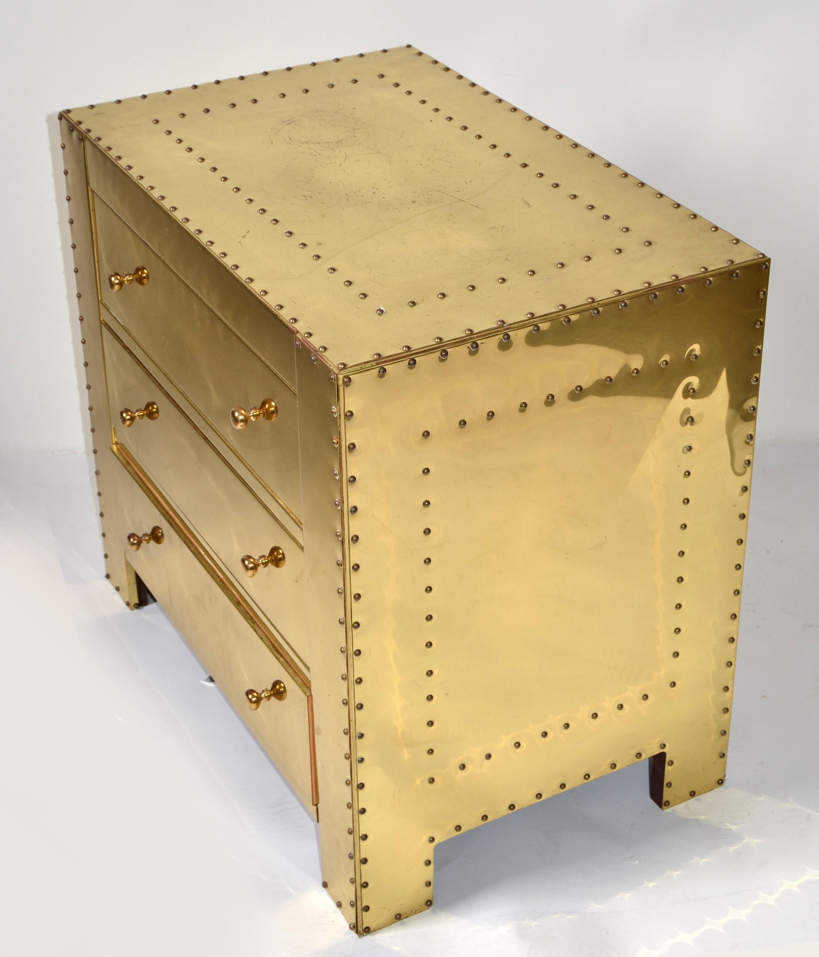 Vintage handsome Asian inspired three drawer riveted brass Nightstand, Bedside Table by Sarreid Ltd.
Small Chest of drawers with a mirrored brass exterior. Features a finish with brass nail head detail throughout. The substantial brass pulls easily